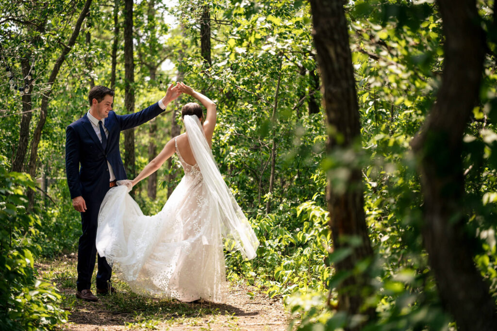 Bride and groom dancing on a forest path, surrounded by lush green foliage.