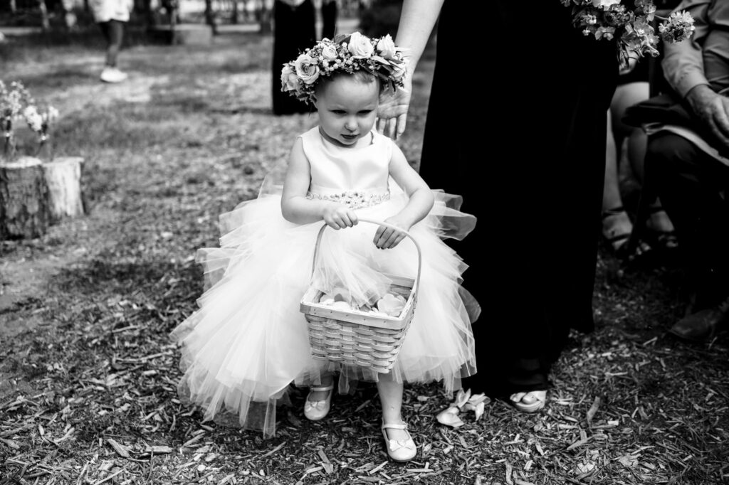 Young girl in a dress and flower crown holds a basket, walking outdoors.