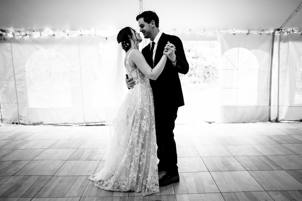 Bride and groom share a romantic dance under a tent, with string lights in the background.