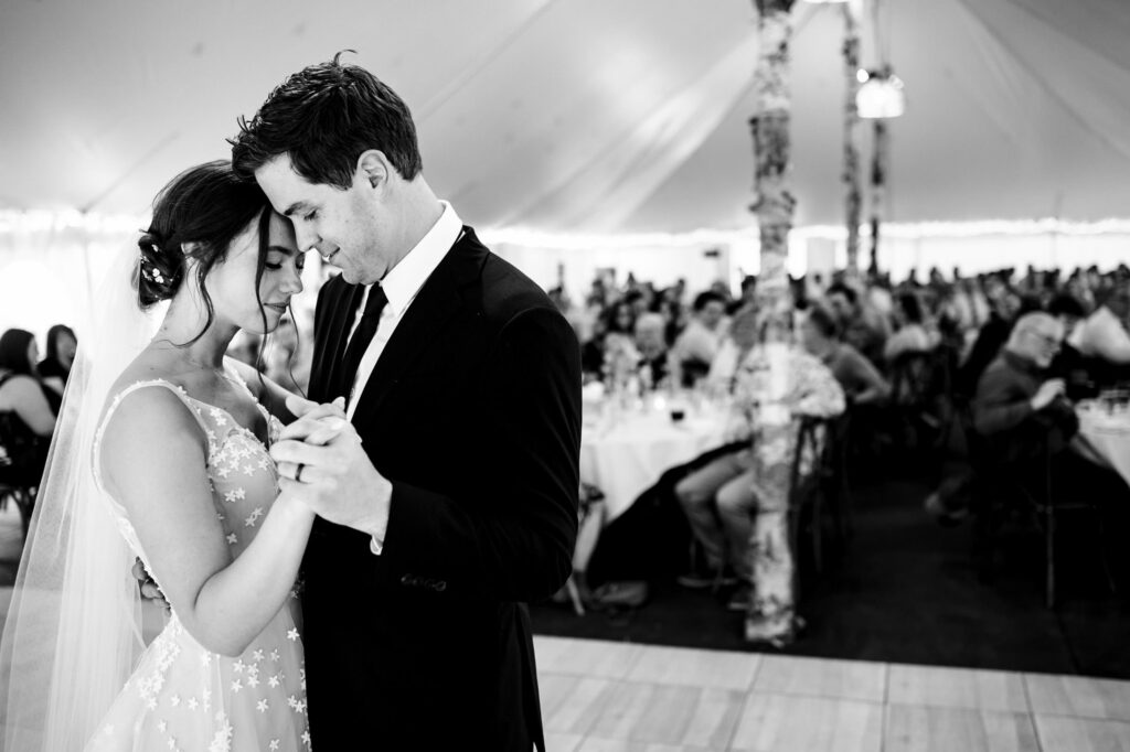 Bride and groom share a dance at their wedding reception under a tent.
