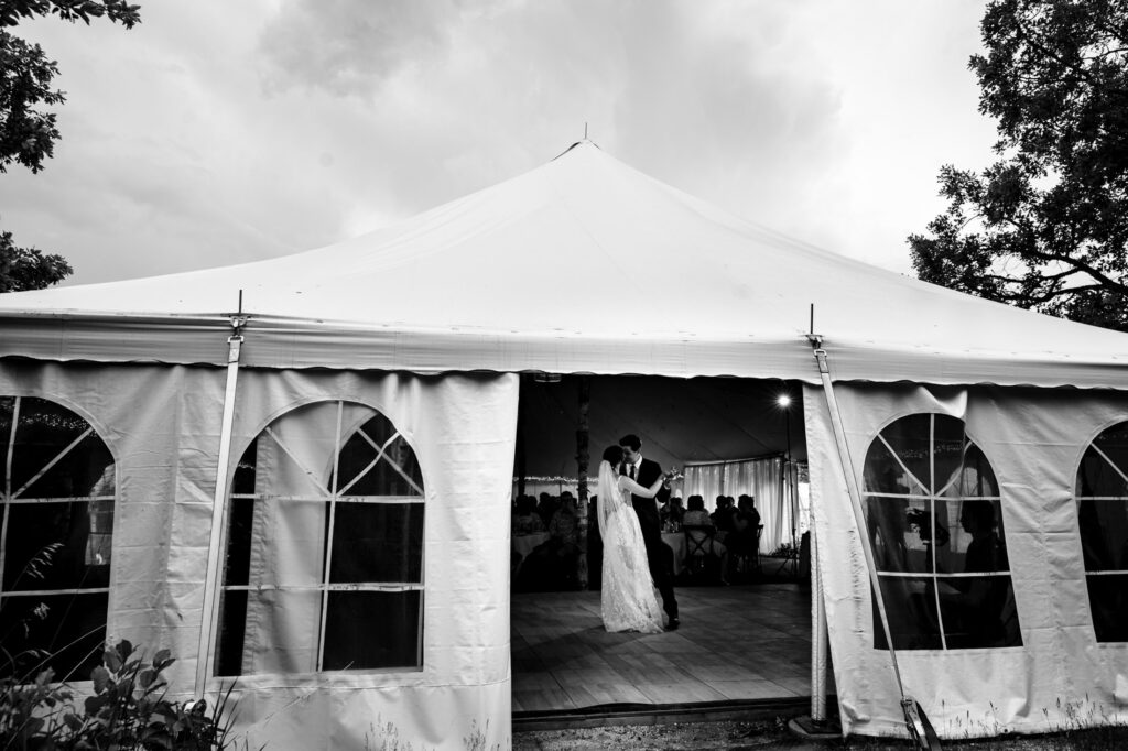 A couple dances inside a large white tent during a wedding reception.