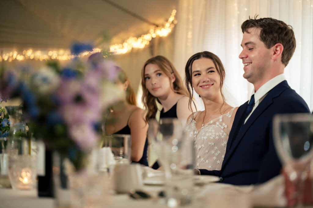 People sitting and smiling at a decorated table with flowers and lights in the background.