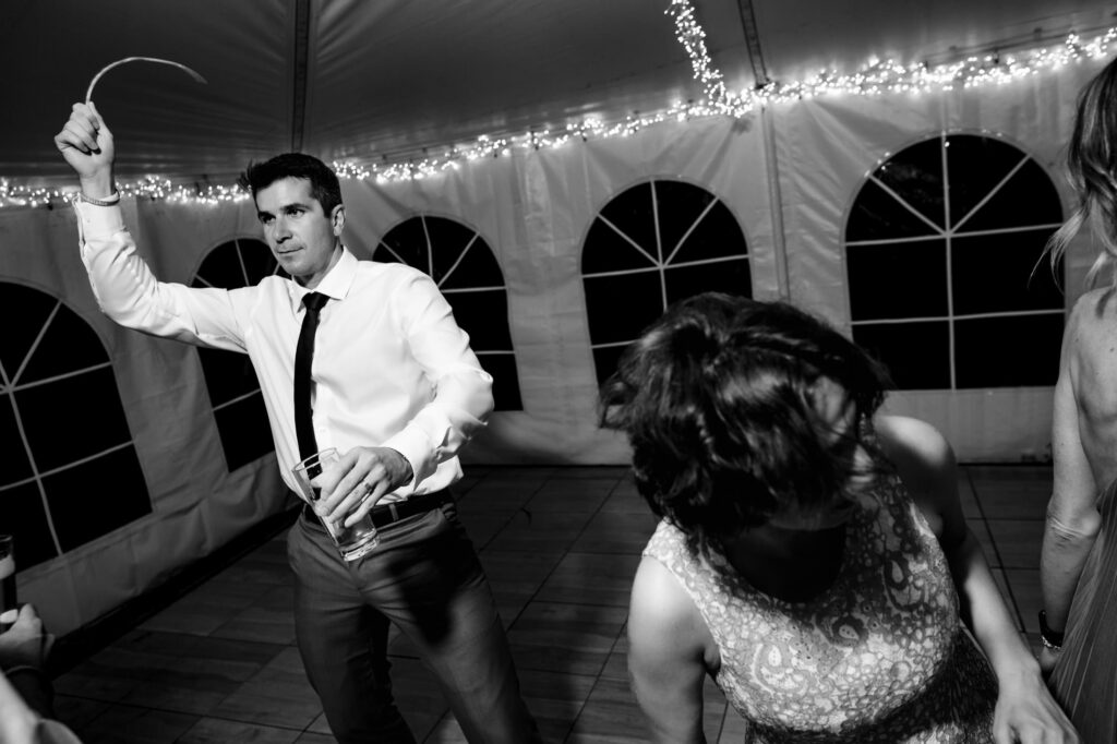People dancing energetically in a tent with string lights.