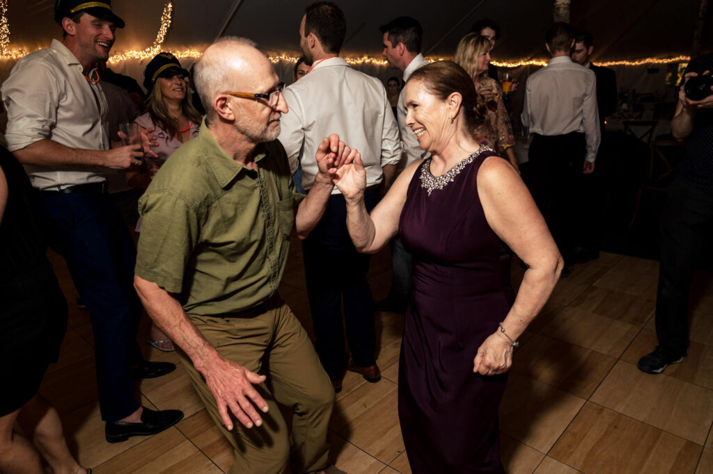 A couple dances joyfully at a lively party under string lights.