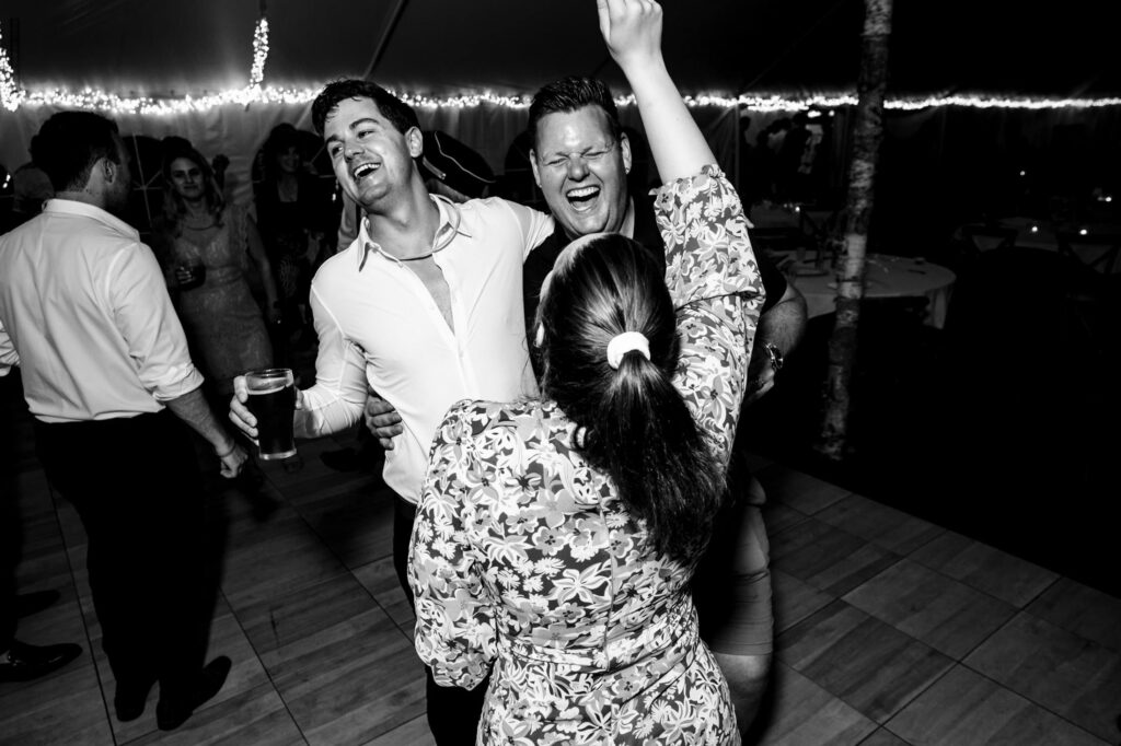 People dancing and laughing at a party, with one holding a drink, in a lively, festive atmosphere.