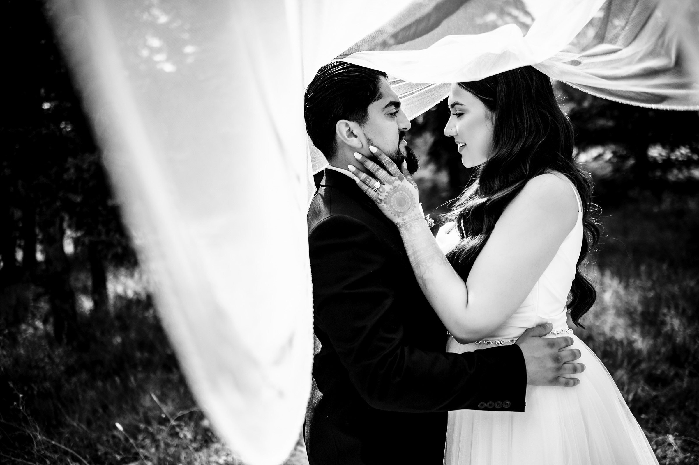 Bride and groom embrace under flowing drapery in a black and white photo.