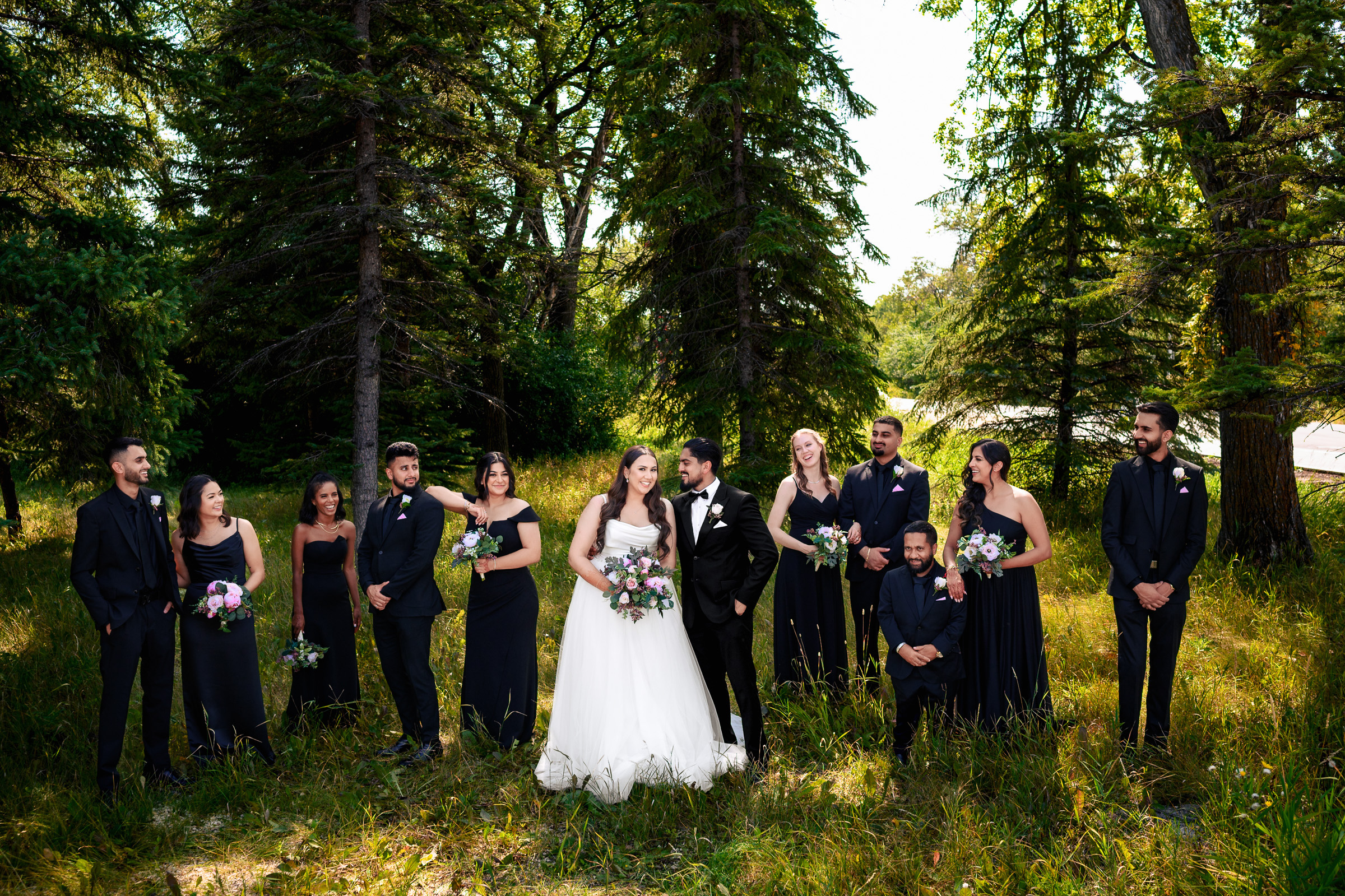 Wedding party posing outdoors in formal attire among trees.