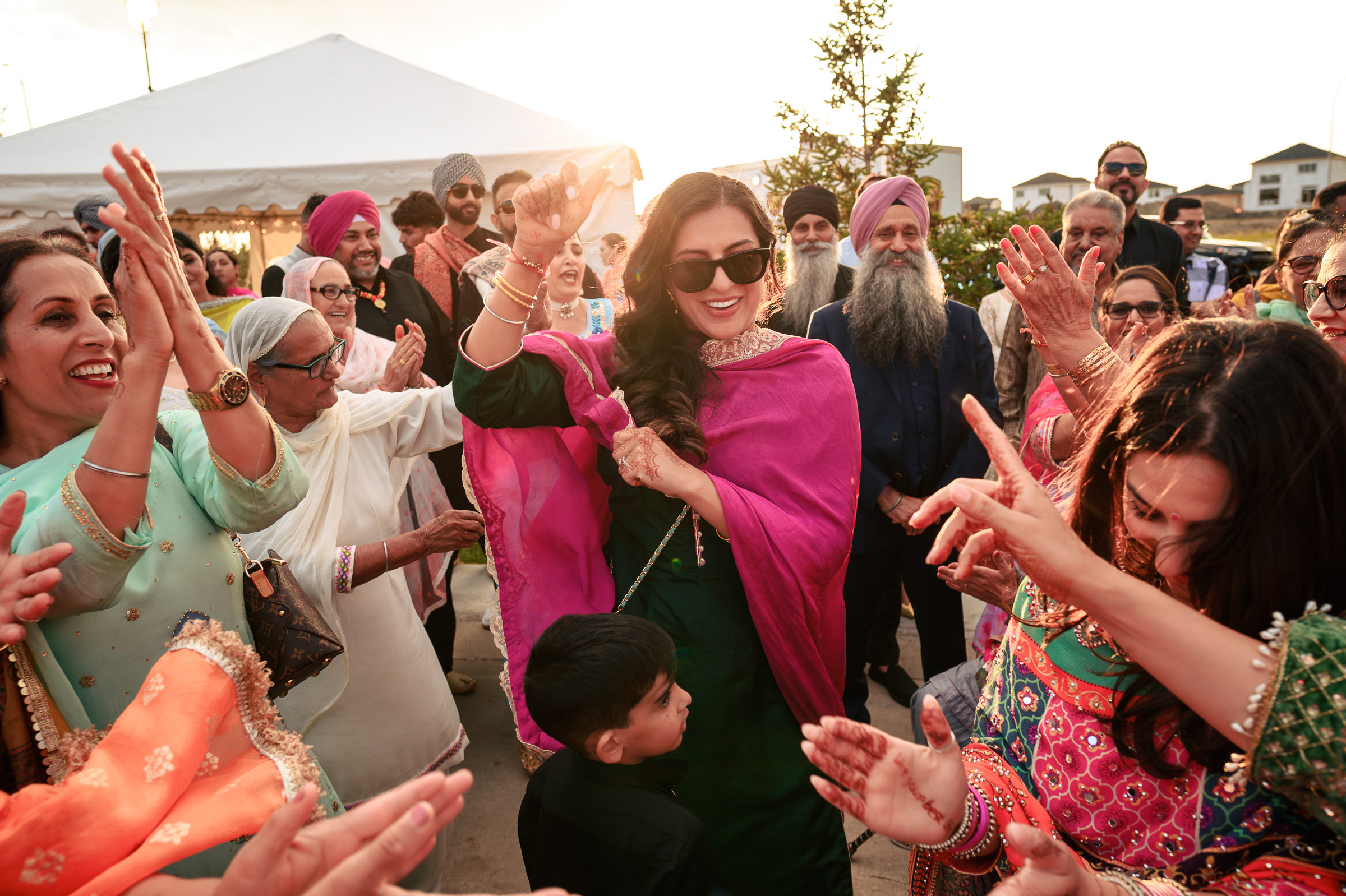 Group of people celebrating outdoors, with some dancing and wearing colorful traditional attire.