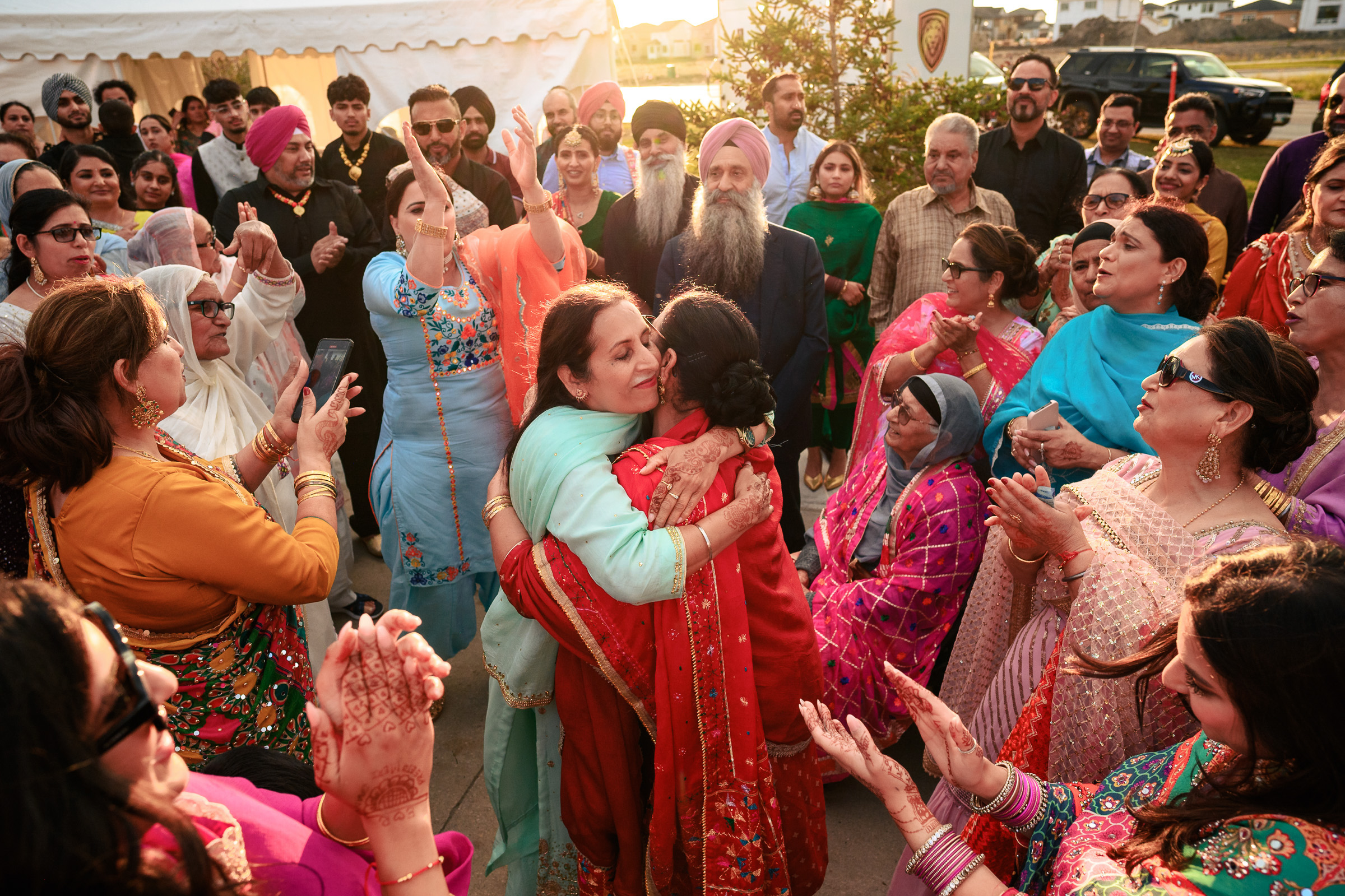 A group of people in vibrant attire celebrate with hugs and clapping outdoors.