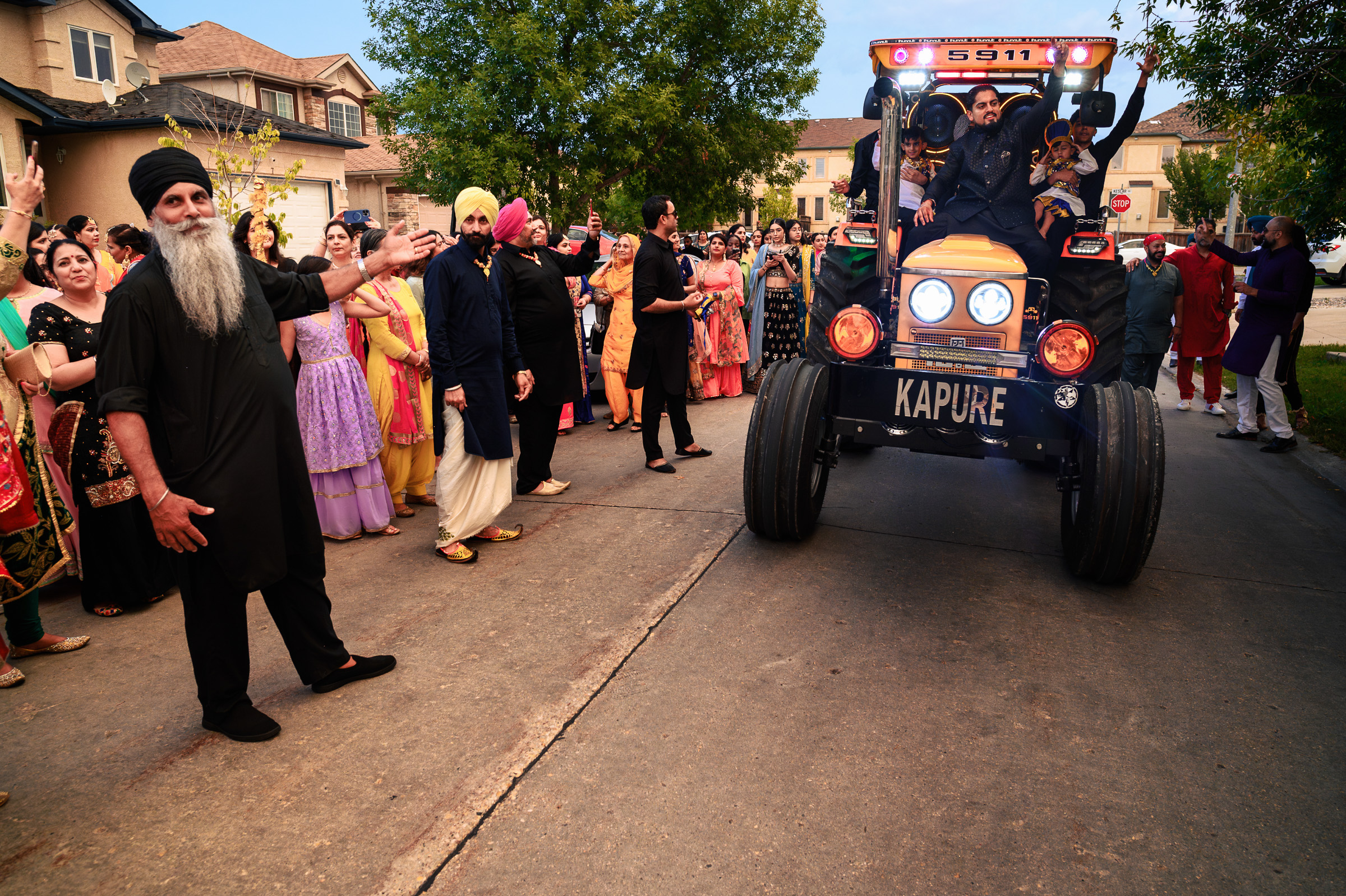 A group of people in festive attire surrounding a small tractor on a suburban street.