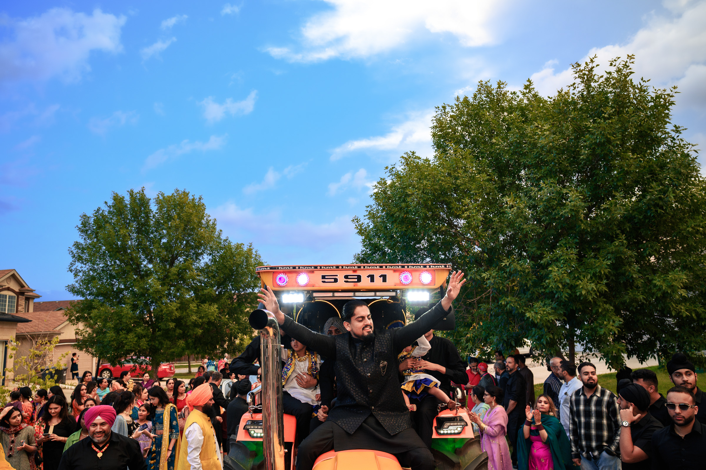 A man in traditional attire stands on a tractor amidst a vibrant outdoor gathering.