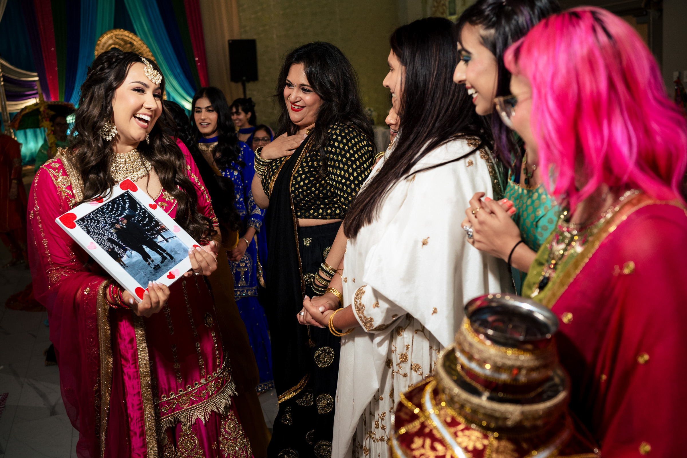 A woman in traditional attire holds a large playing card, surrounded by others in colorful dresses.