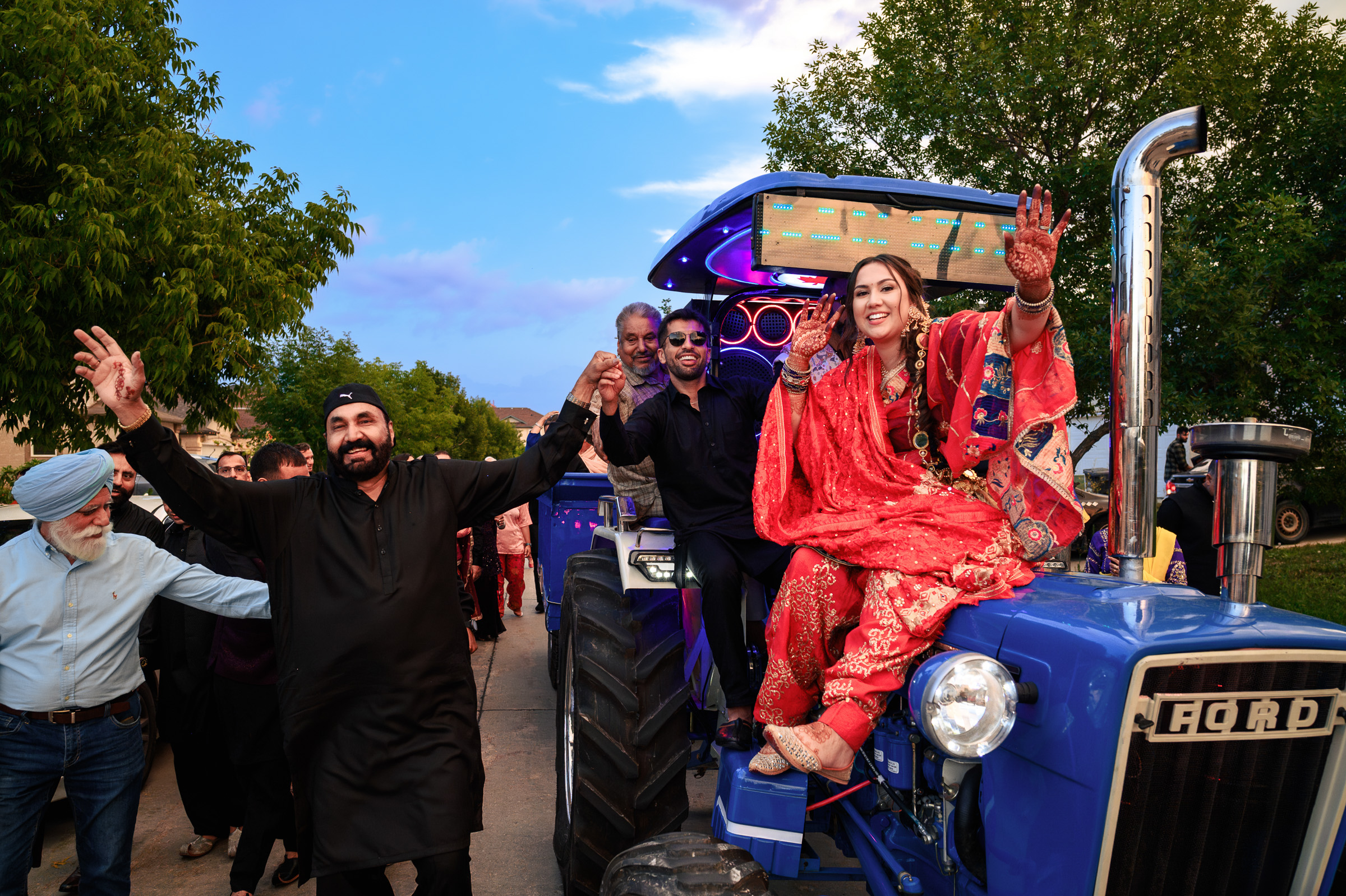 Group celebrating on and around a blue tractor, with a woman in red attire seated on it.