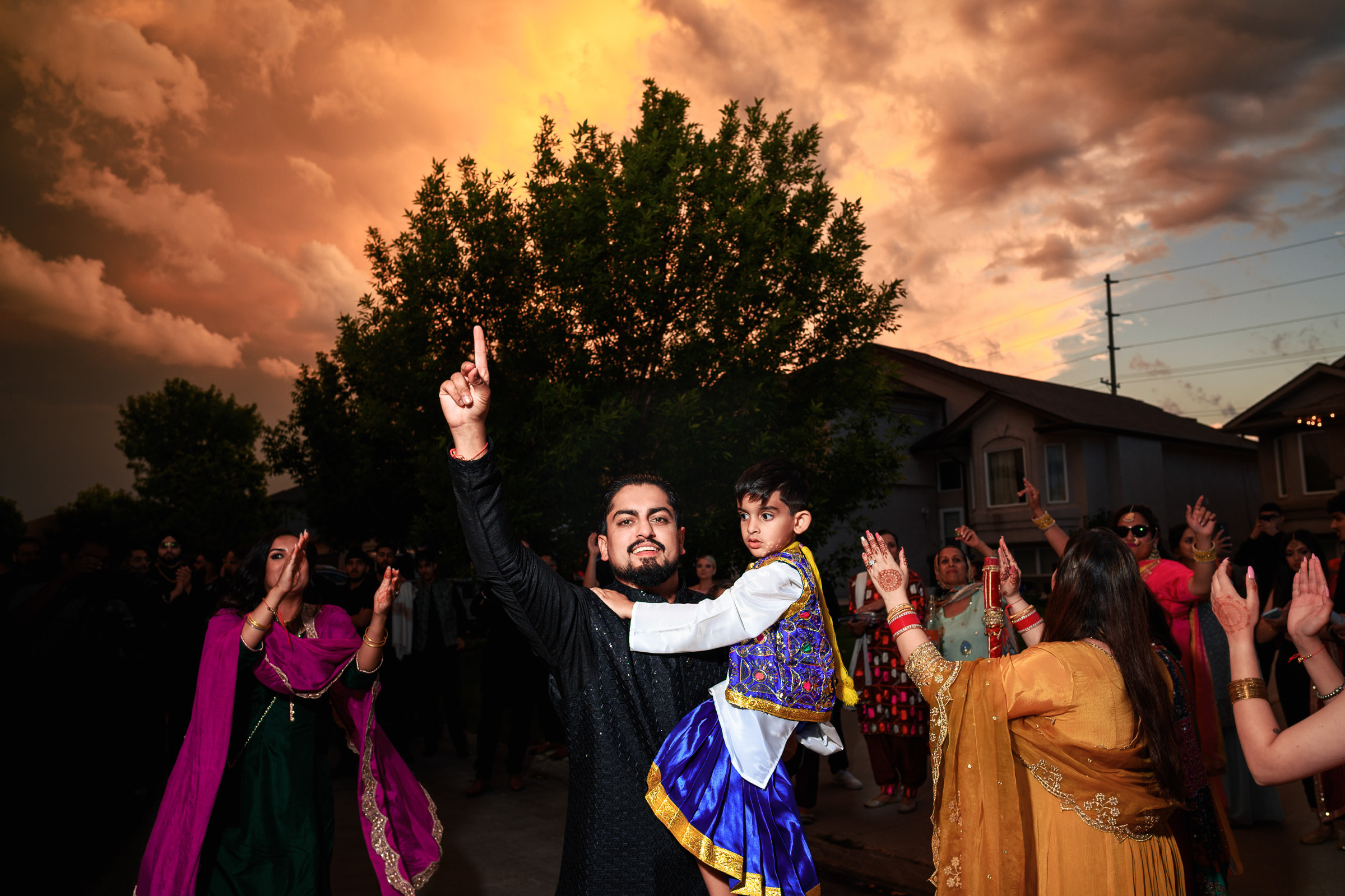 Man holding child, pointing upwards during outdoor celebration under dramatic sky.