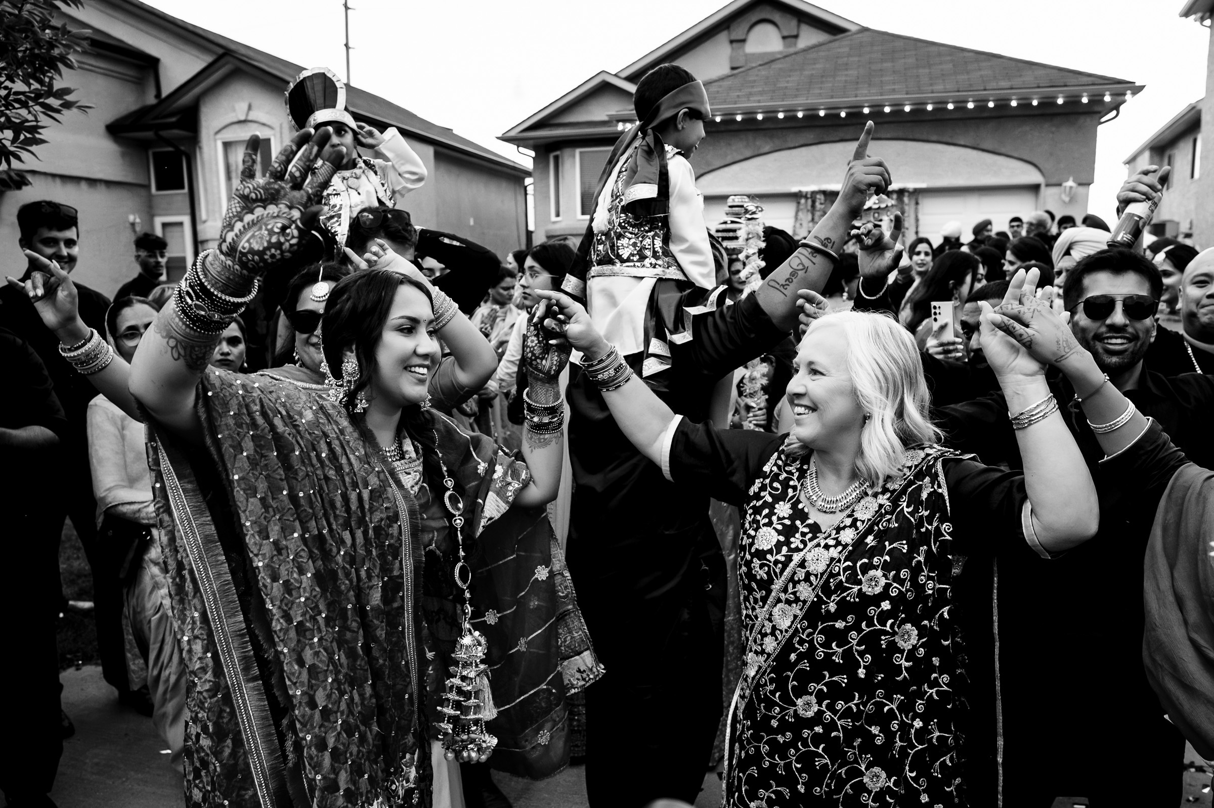 Two women joyfully dance at a lively outdoor celebration, surrounded by a crowd.