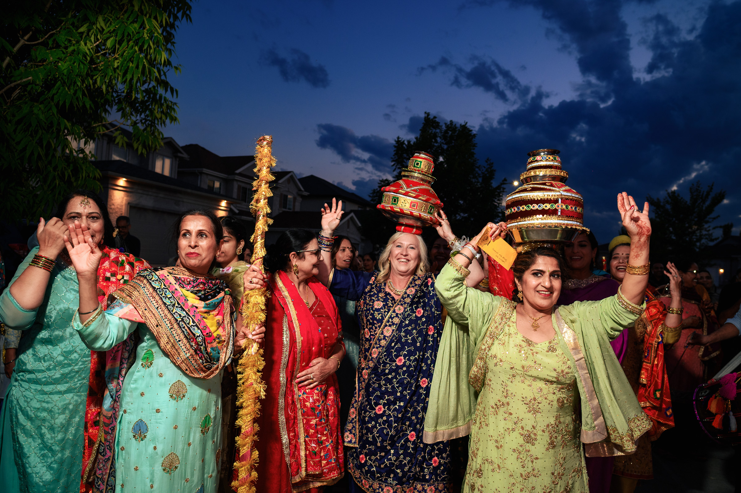 Women celebrating with baskets on heads, wearing colorful traditional attire at dusk.