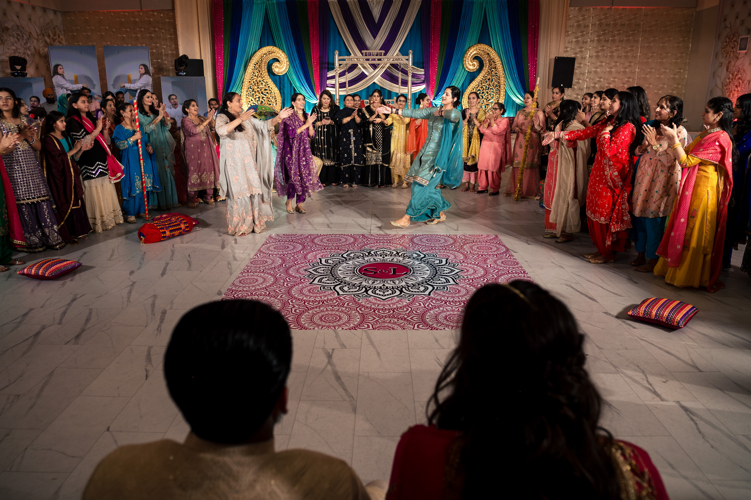 A couple watches a group dance performance at a colorful indoor cultural event.