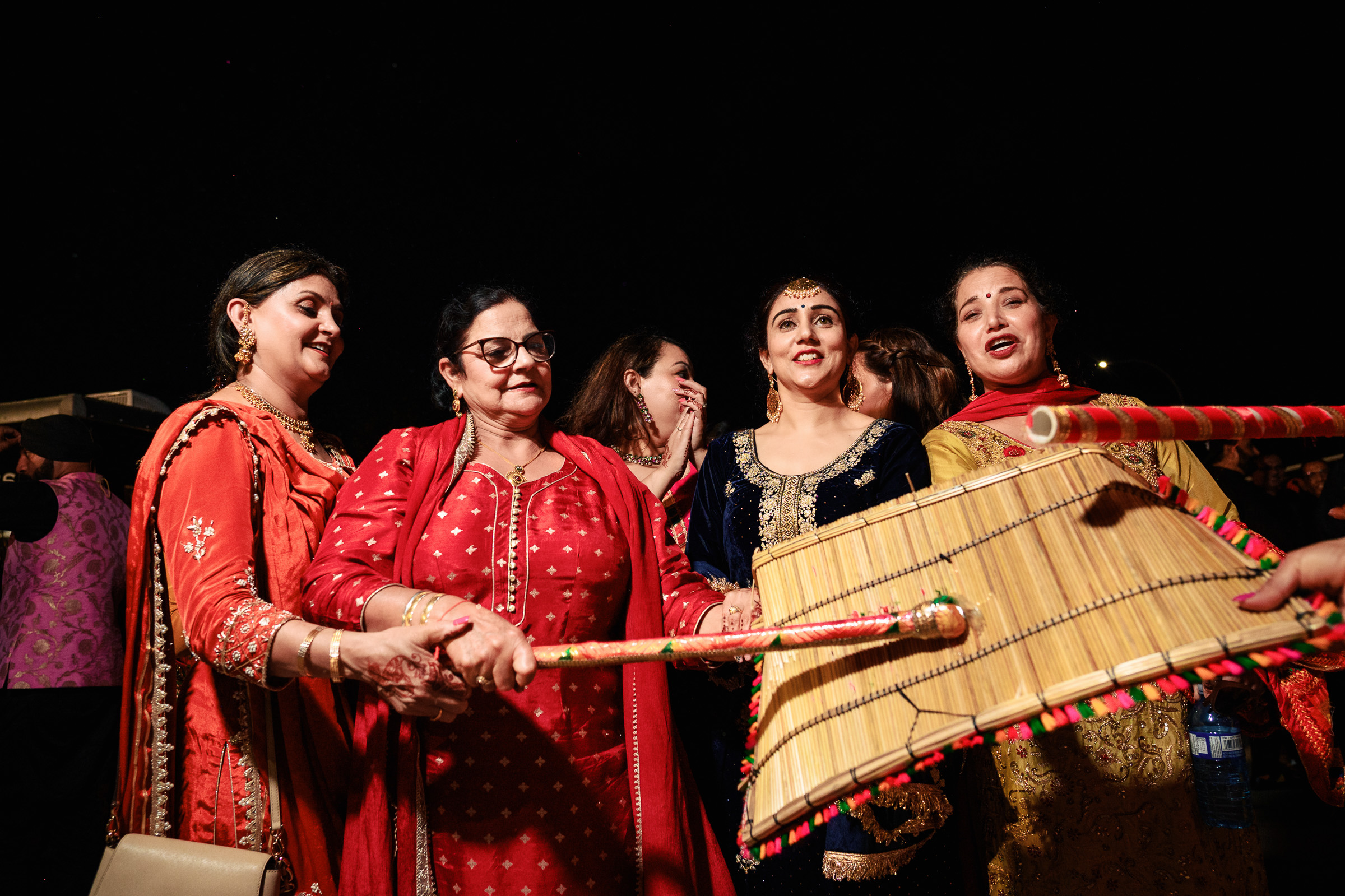 People in traditional attire dancing with sticks and mats at a nighttime celebration.