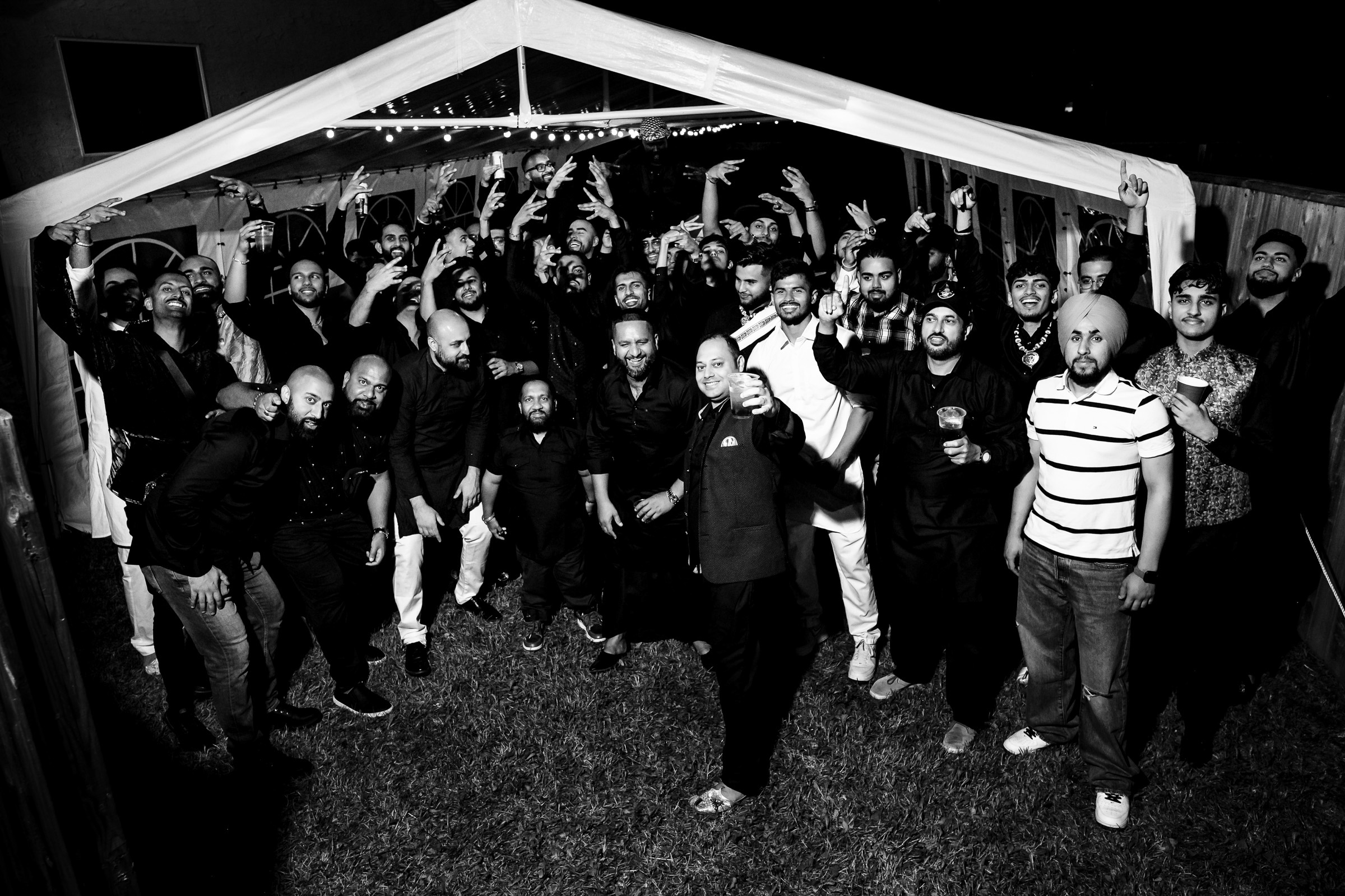 Group of people posing and gesturing under a tent at night.