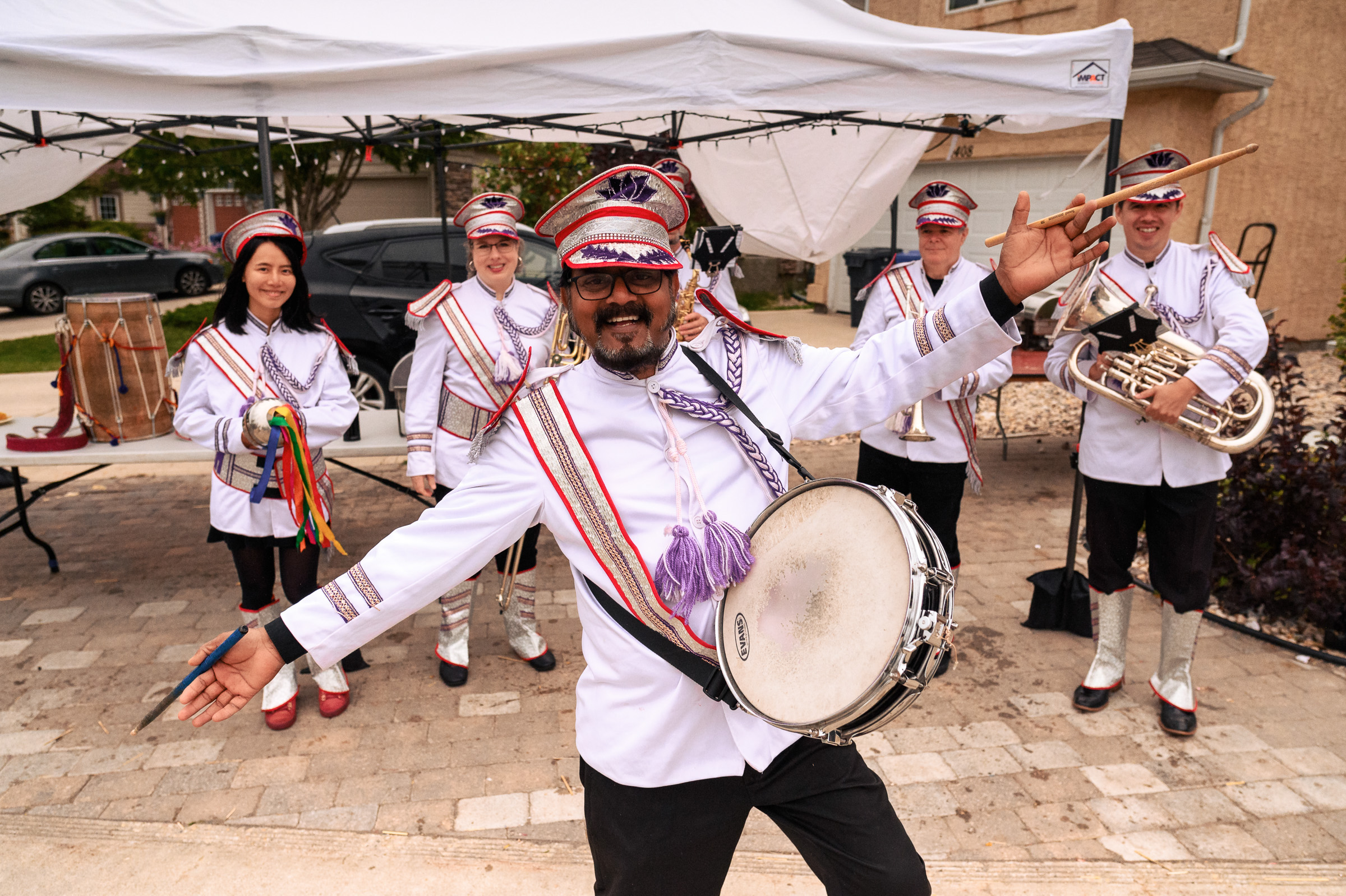 A marching band in uniform poses with instruments and smiles under a canopy.