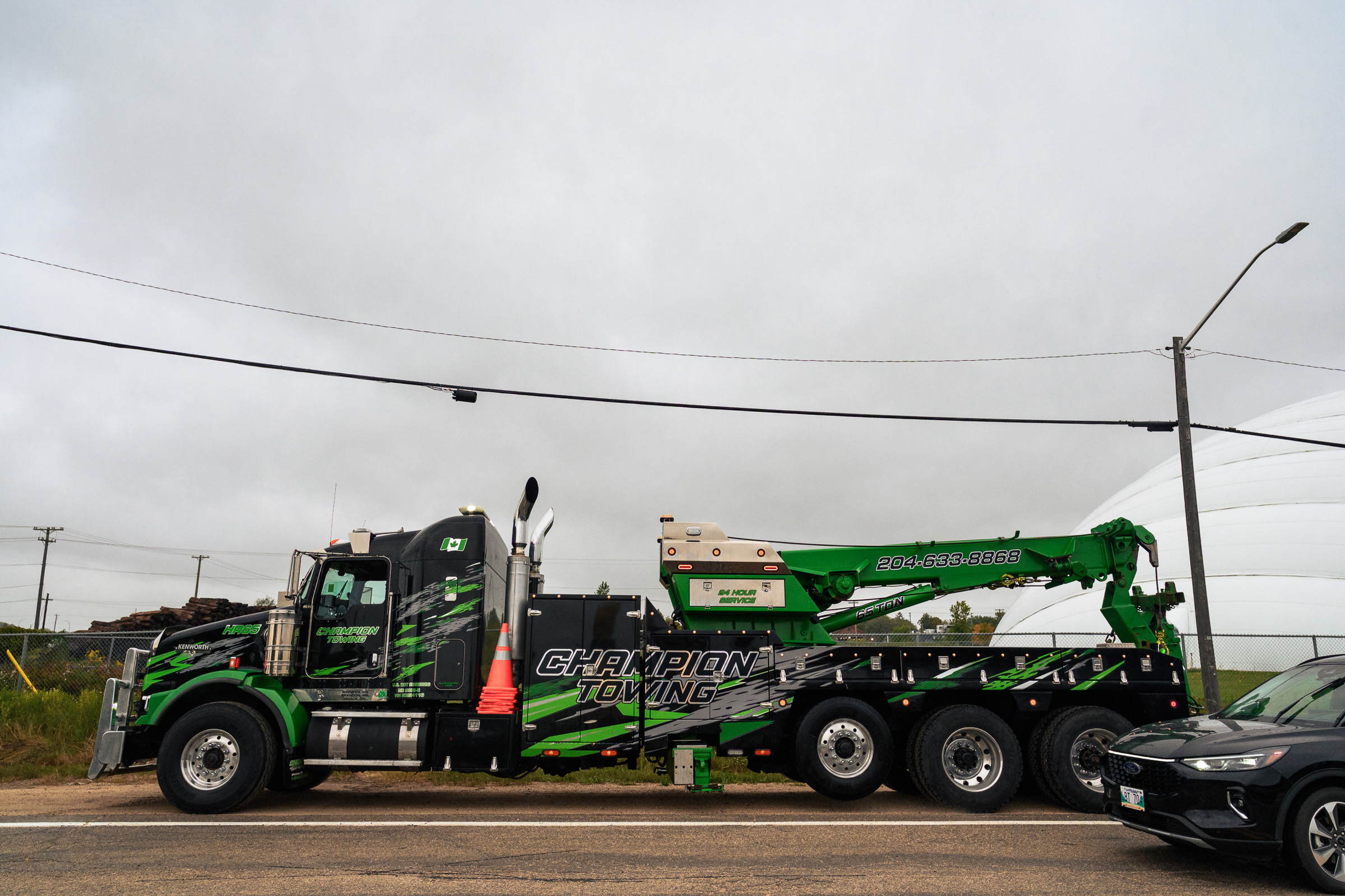 Green and black tow truck parked on the road in front of a white building.