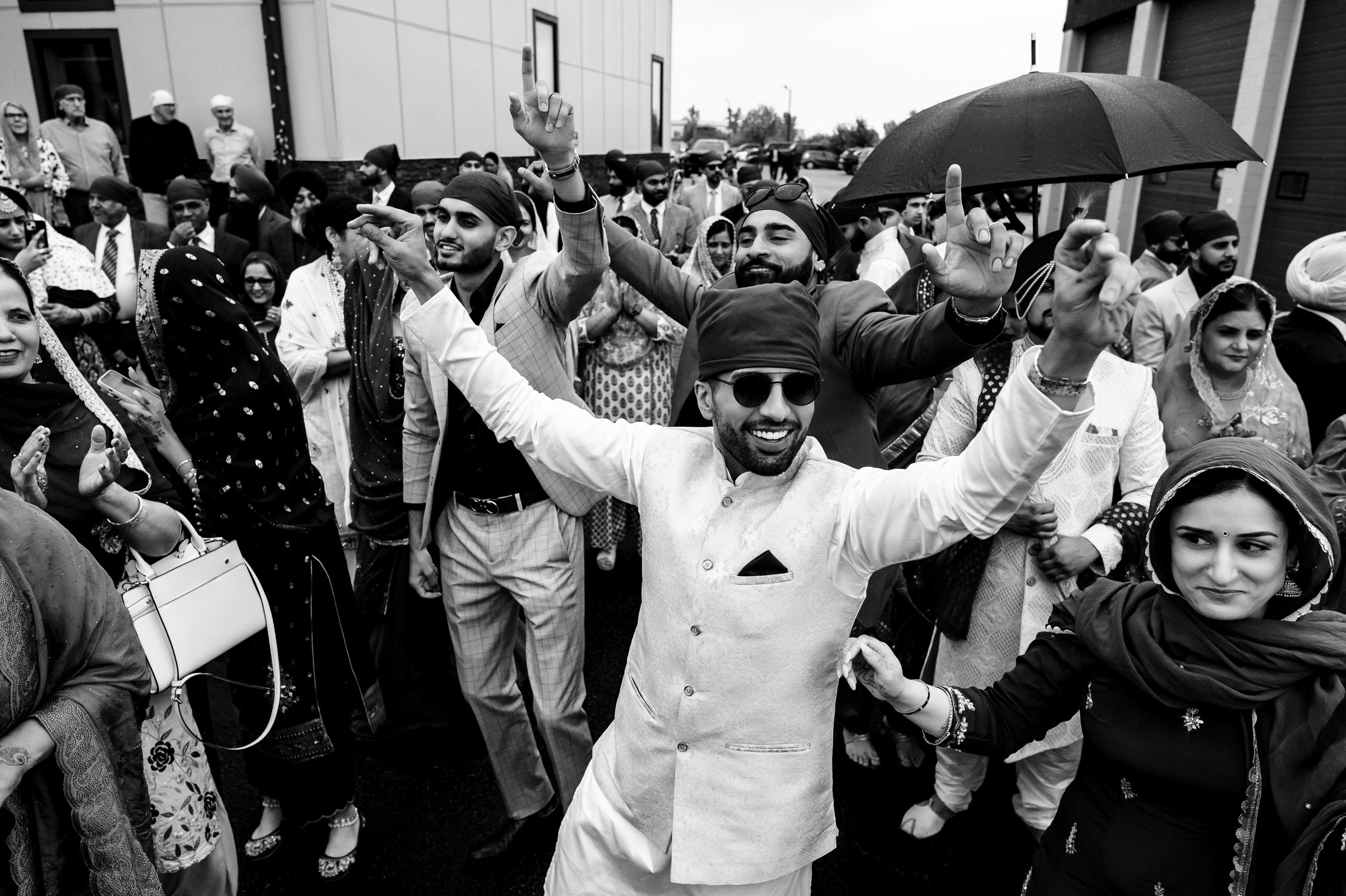 People dancing and celebrating outdoors, with one person holding an umbrella.