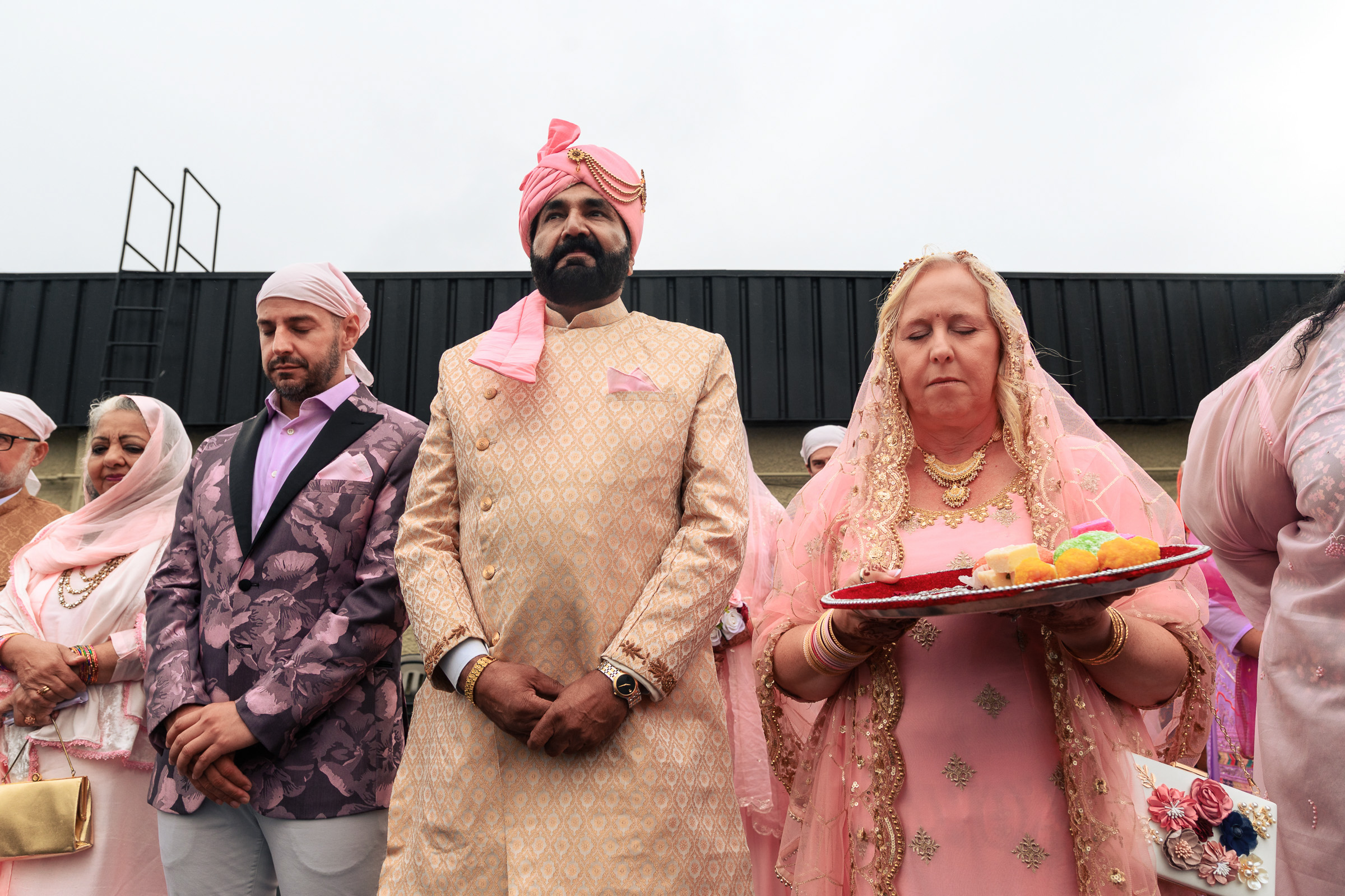 Group in pink and gold attire standing; one holds a tray with colorful items.