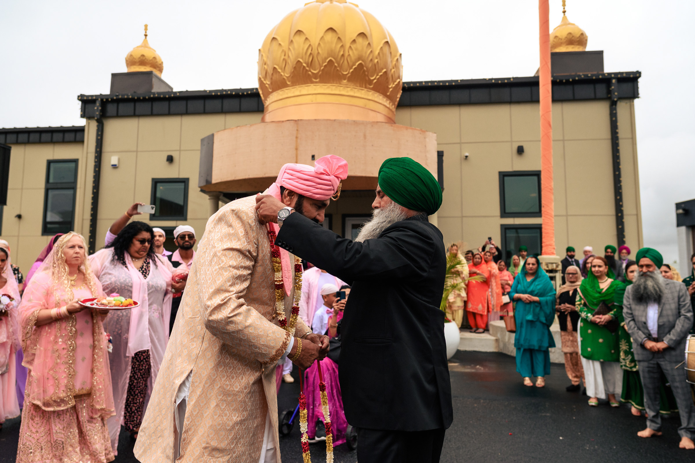 A man in traditional attire being adorned with a necklace outside a temple.