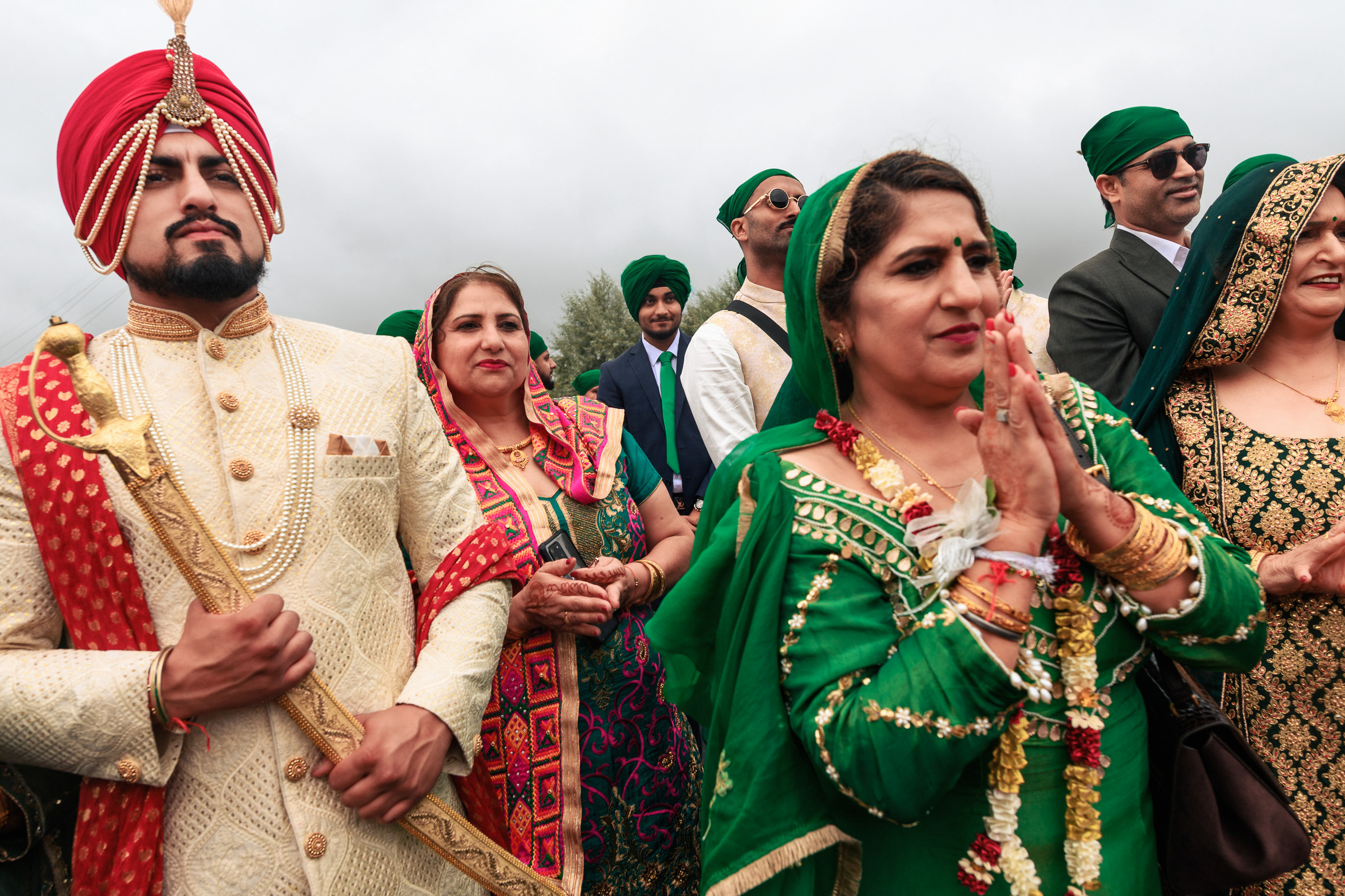A group of people in traditional attire, some in green, standing outdoors at an event.