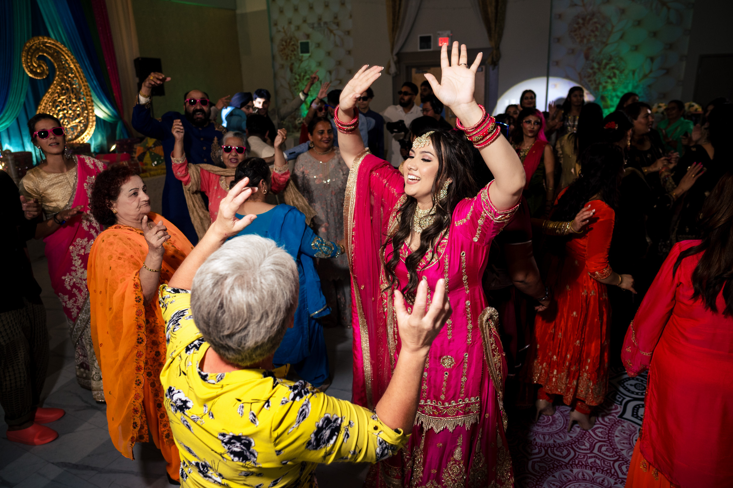 People joyfully dancing in colorful traditional attire at a lively indoor event.