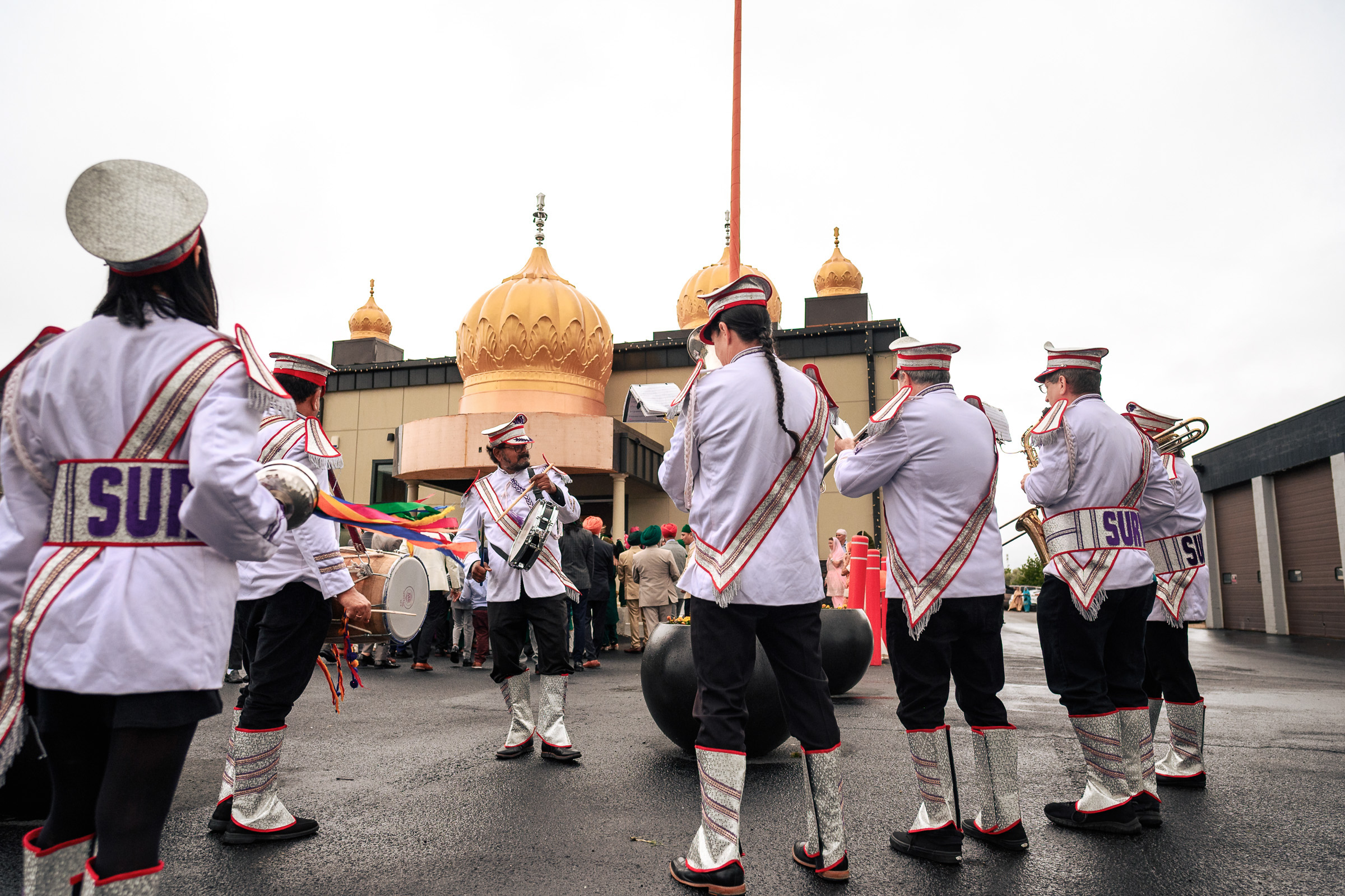 Band in uniform performs outside a building with ornate domes on a cloudy day.