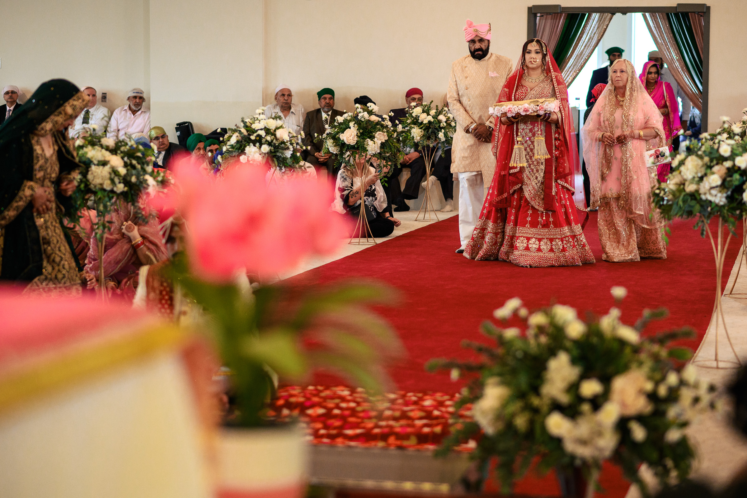 Bride and groom in traditional attire walking down a decorated aisle with family.