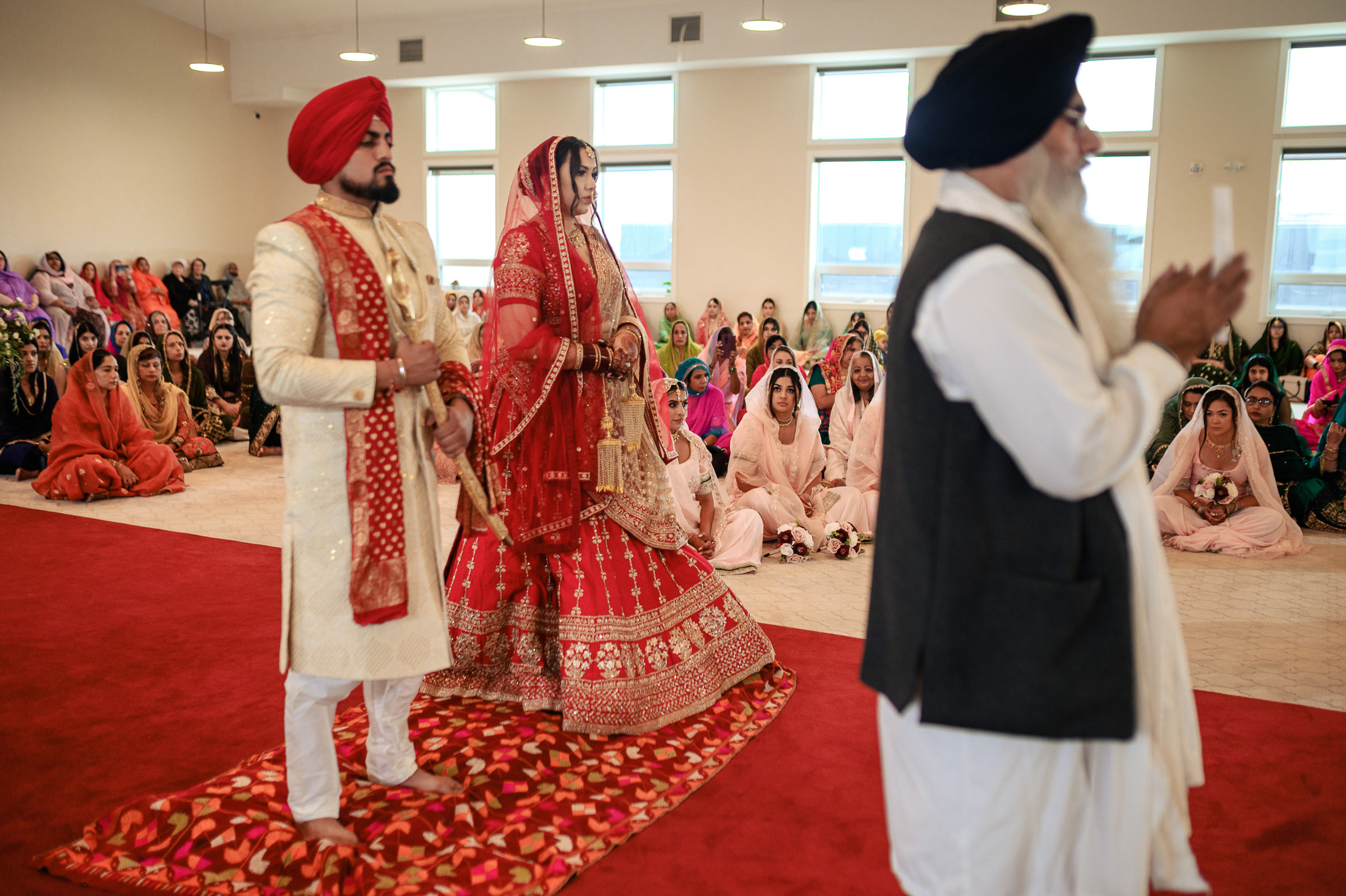 Couple in traditional attire participating in a Sikh wedding ceremony indoors.