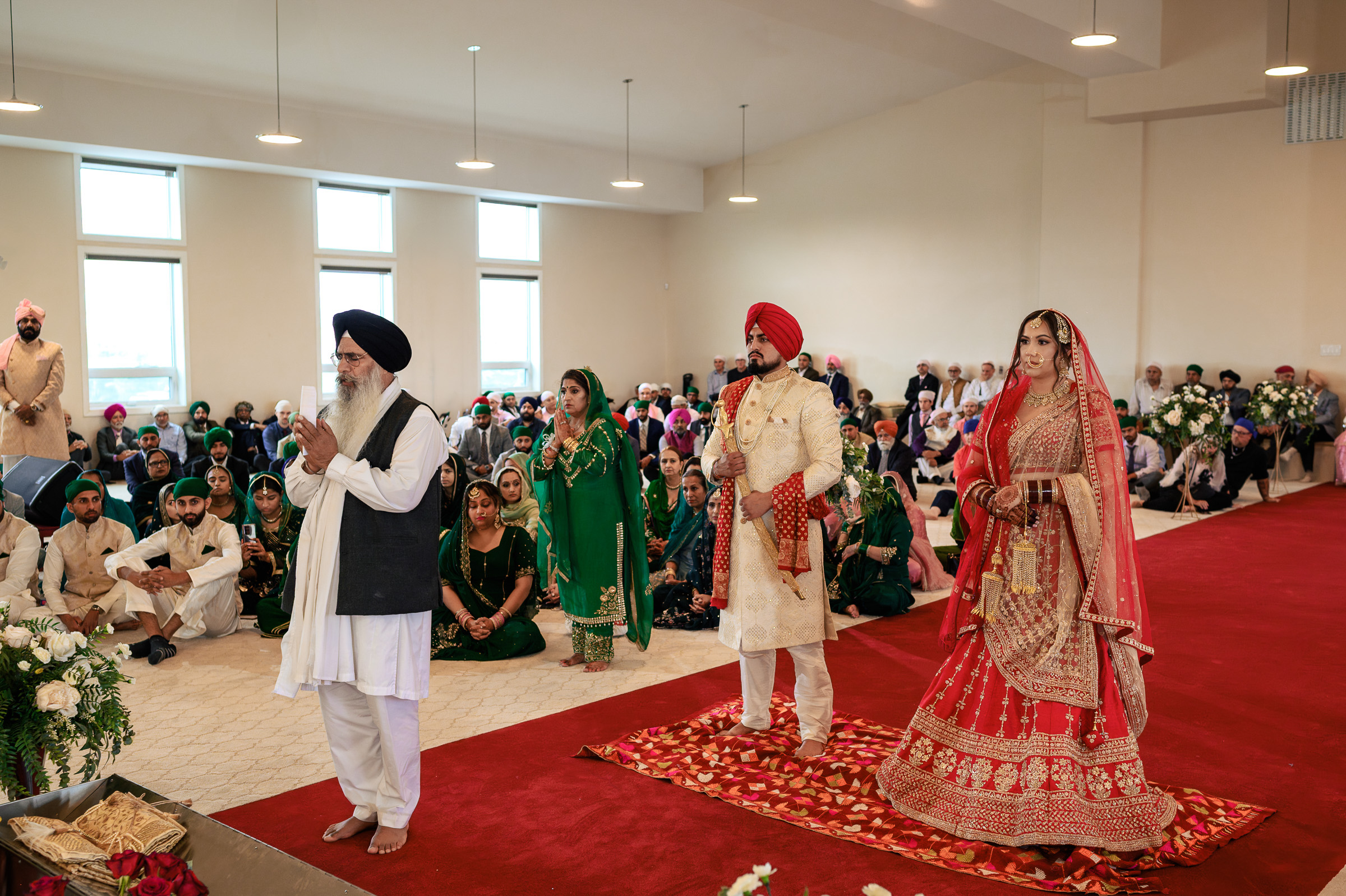 A Sikh wedding ceremony with a couple in traditional attire standing before a group.