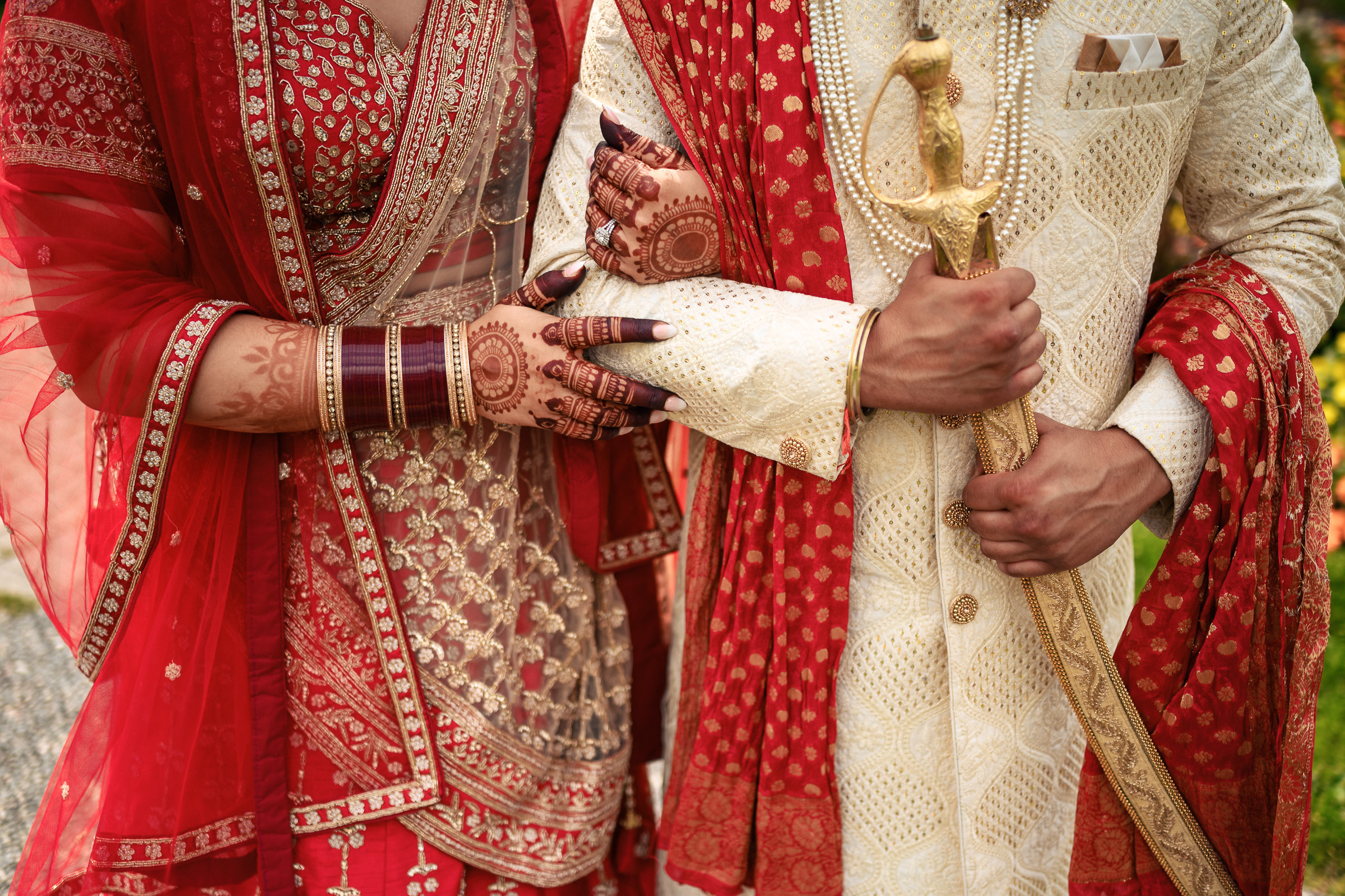 Couple in traditional red and gold wedding attire, holding hands and a ceremonial sword.