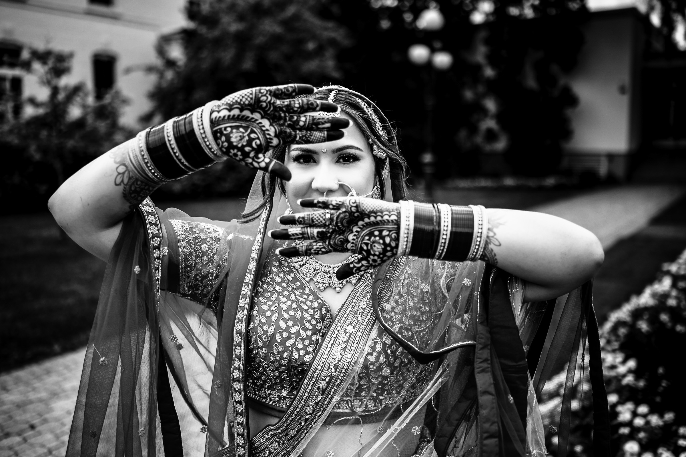Person in traditional attire showing henna-decorated hands in a garden setting.