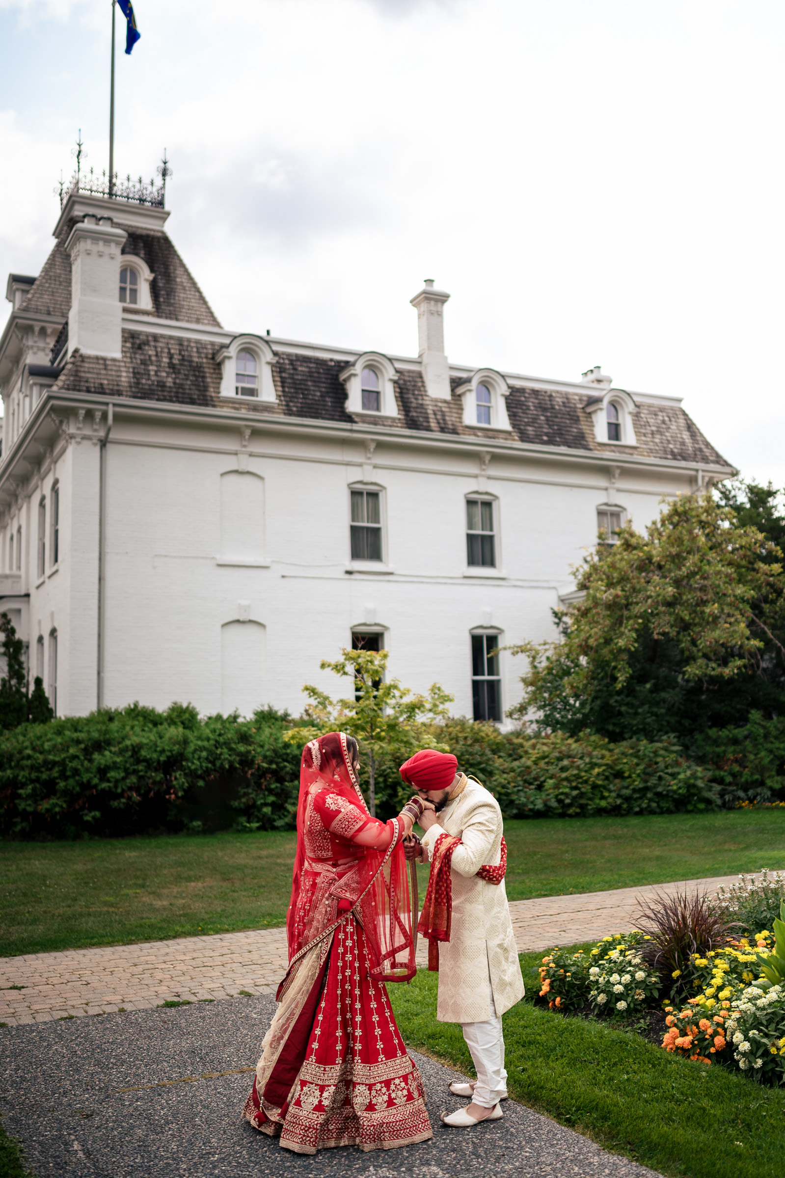 Couple in traditional attire standing in front of a large white building with greenery.