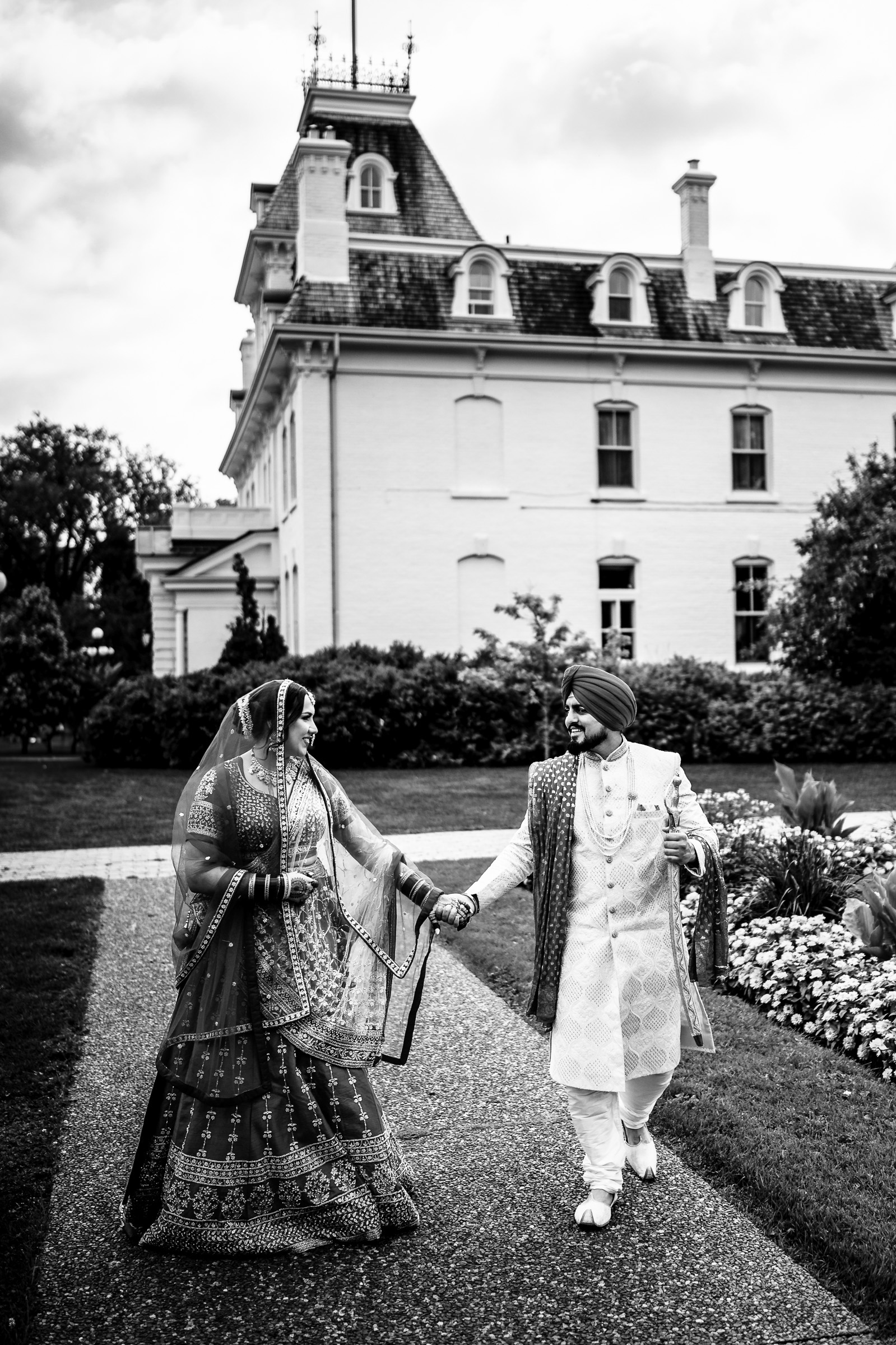 A couple in traditional attire walks hand in hand outside a large building.