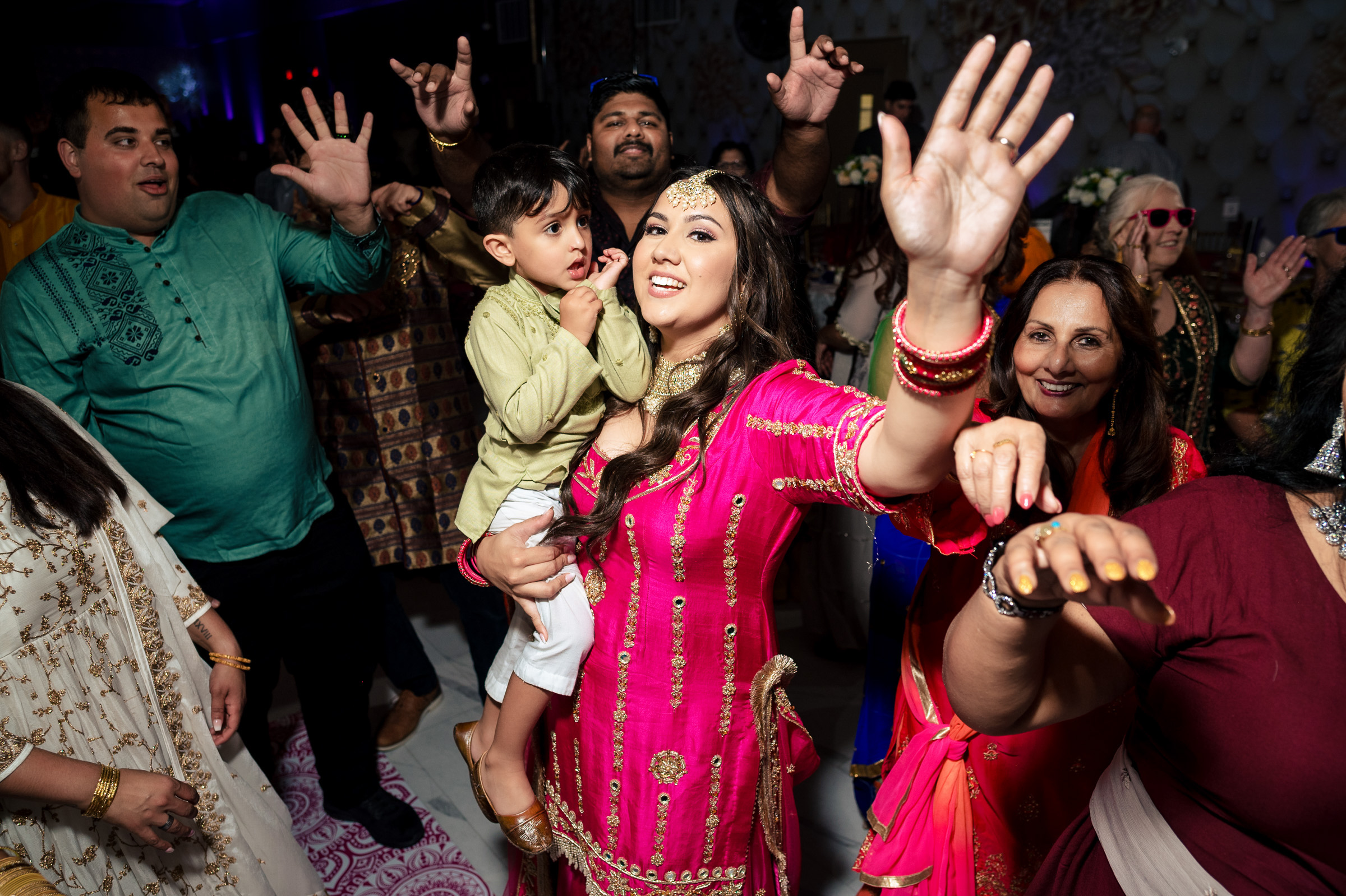People dancing joyfully at a festive event, with a woman in pink holding a child.