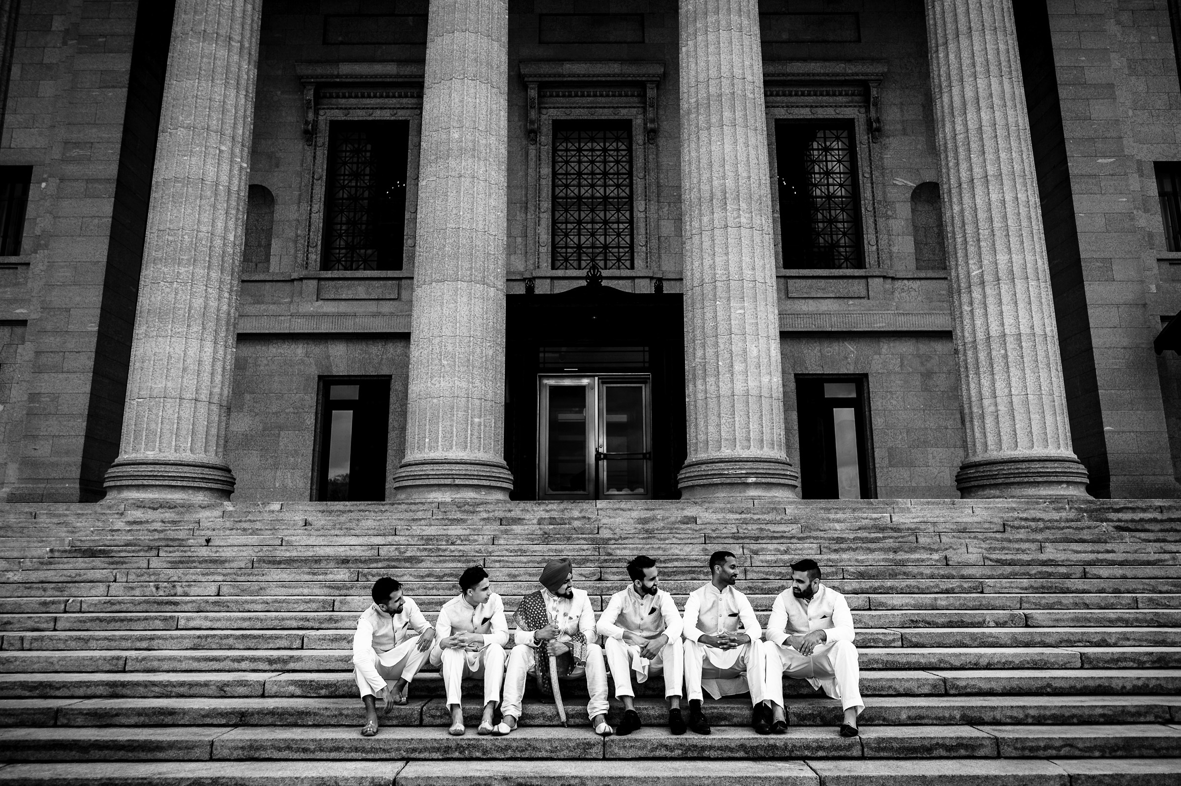 Six men in traditional attire stand in front of a building with tall columns.