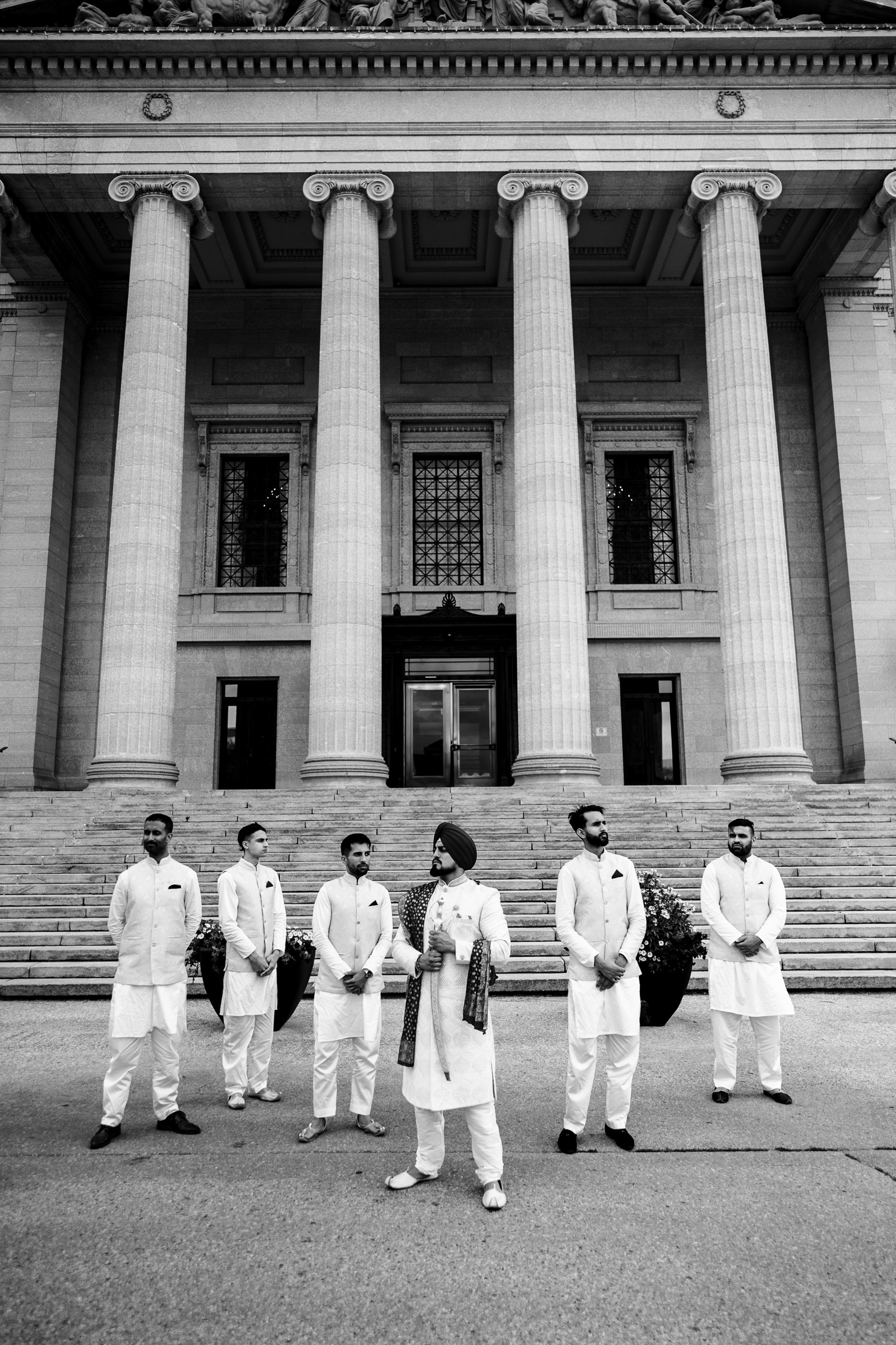 Six men in traditional attire stand in front of a building with tall columns.