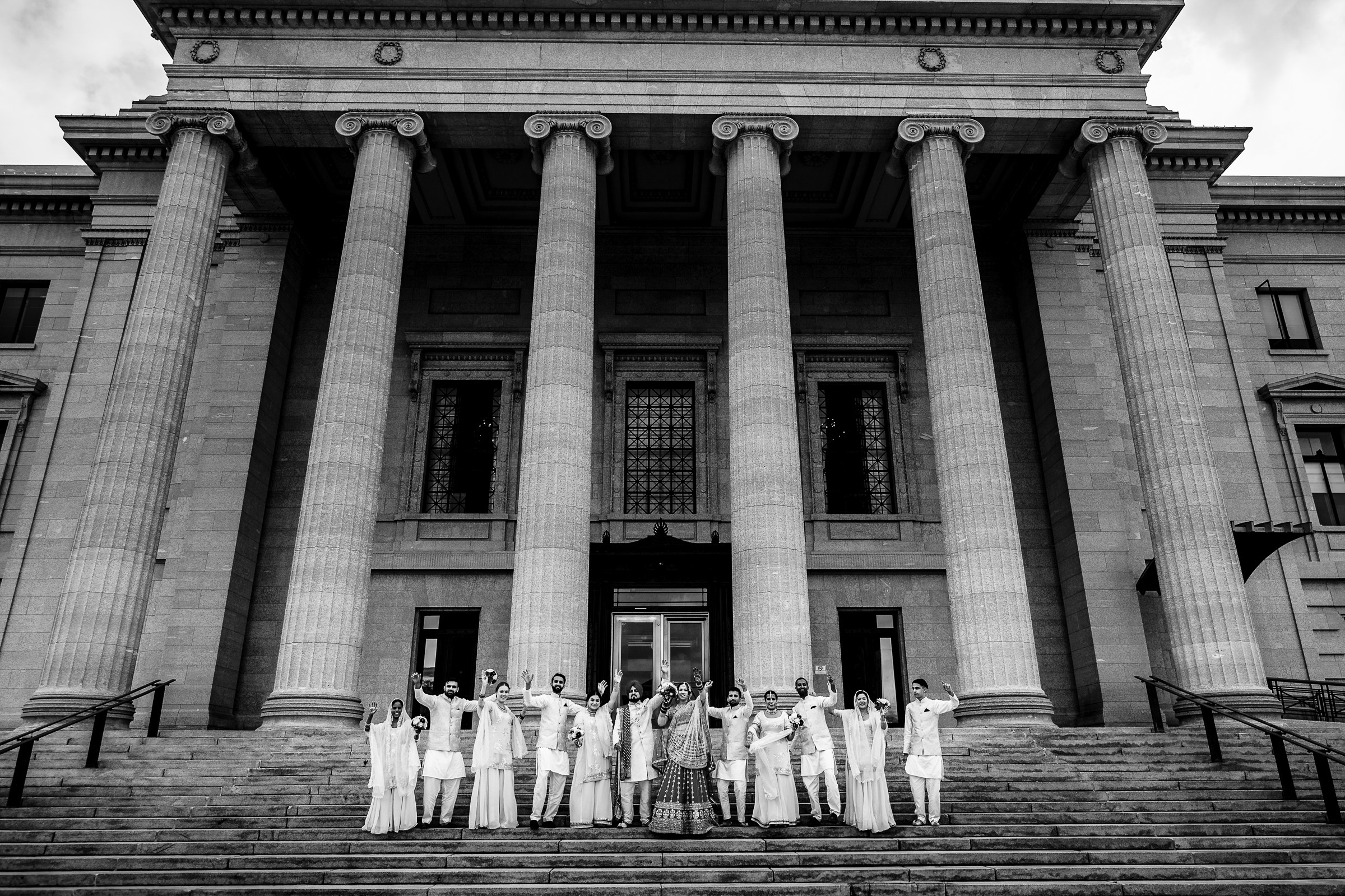Group of people in white outfits stand on stairs of a building with large columns.