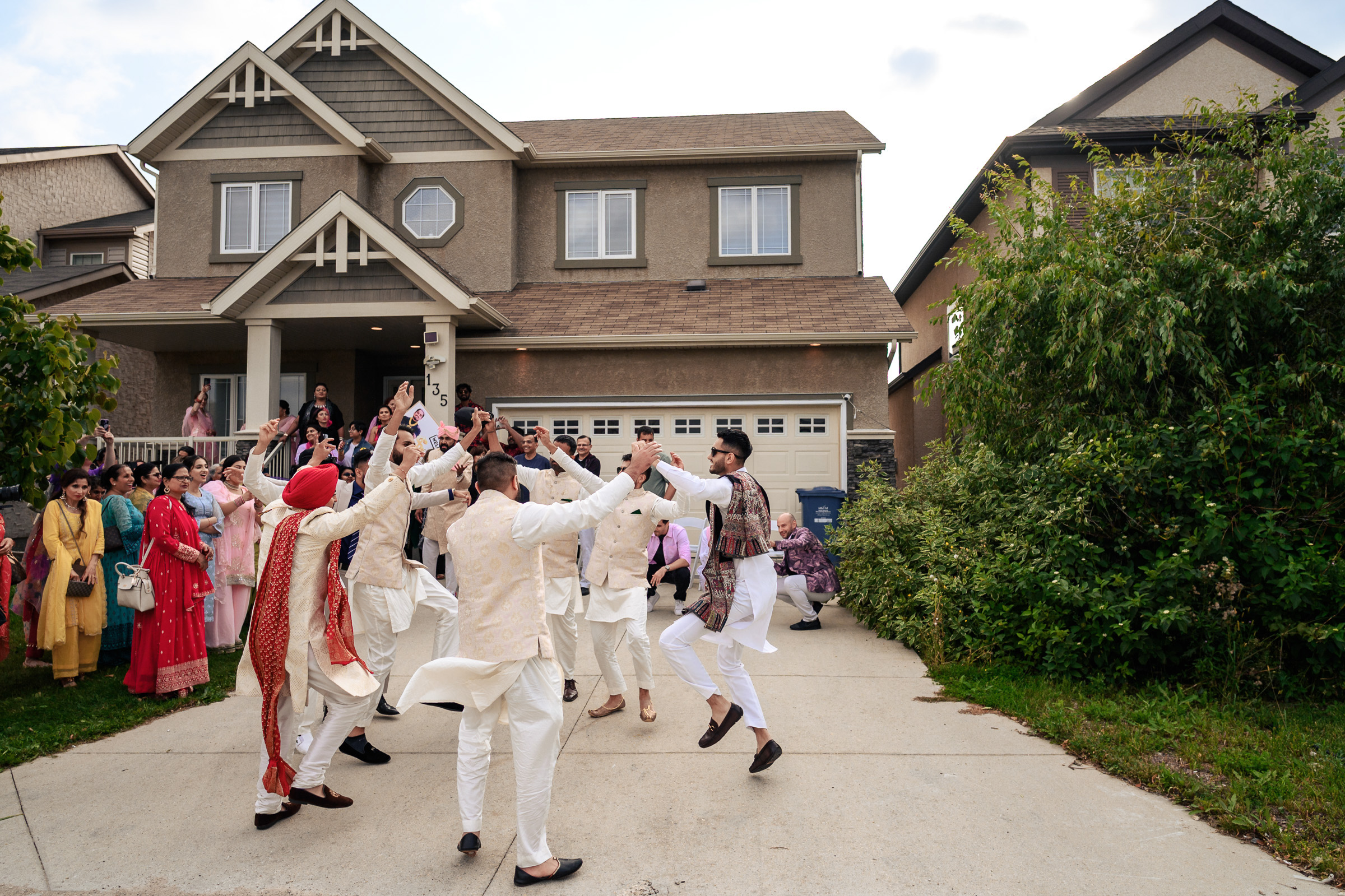 Group of people in traditional clothing dancing joyously outside a house.