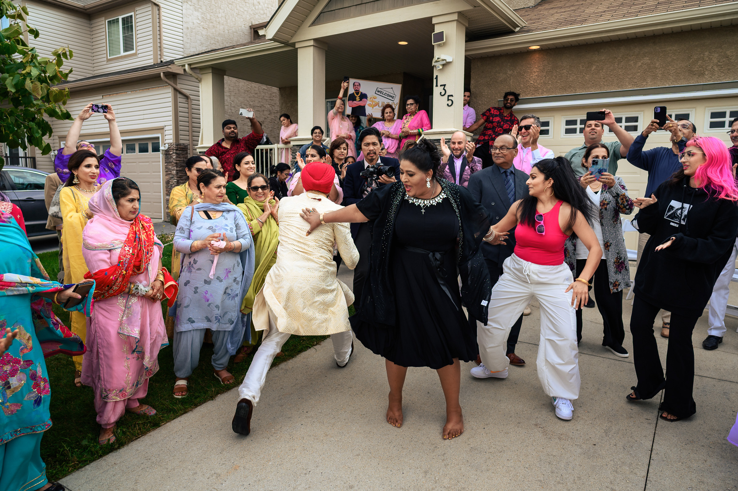 A lively group celebration with dancing participants in colorful attire outside a house.