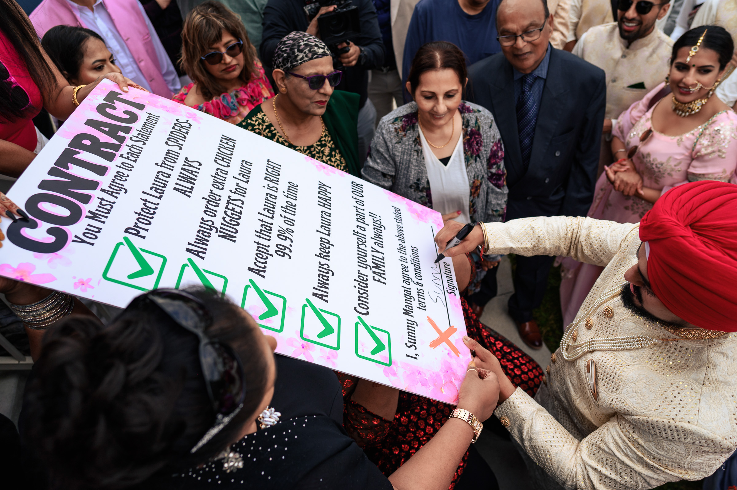 Person signs a large contract board while surrounded by a group of people at an event.
