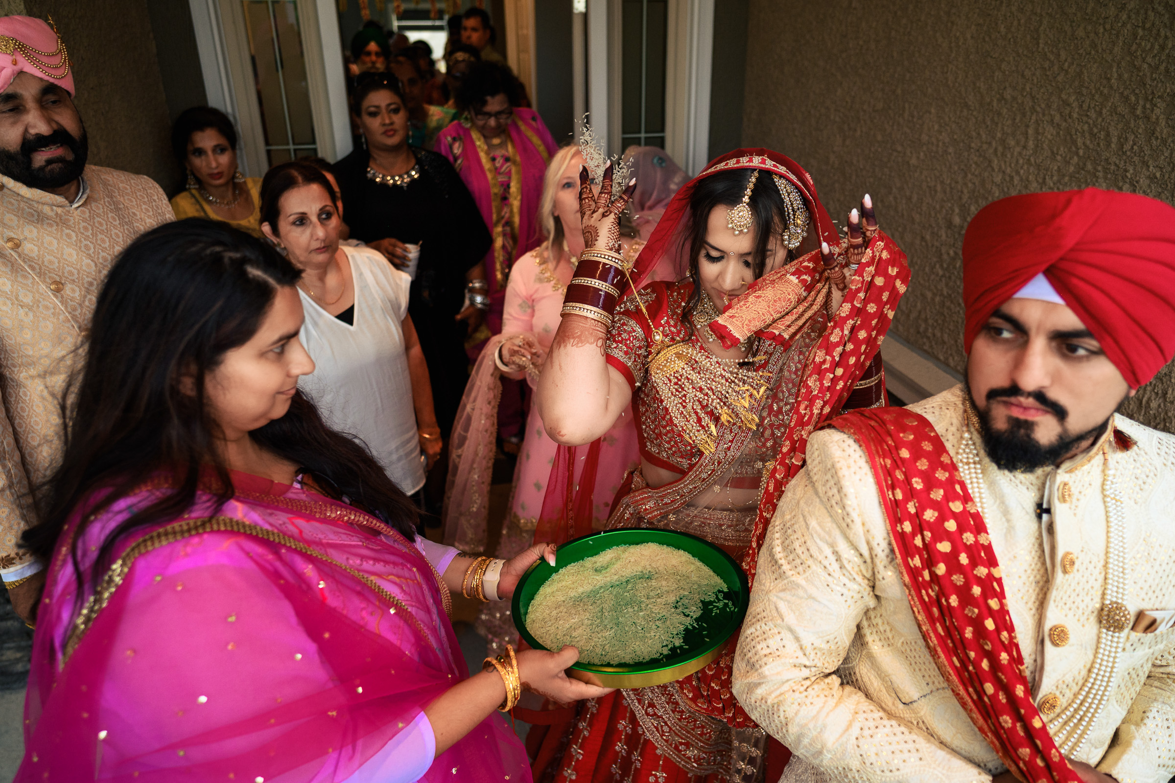 A bride in traditional attire performs a ritual with a tray of rice during a wedding ceremony.