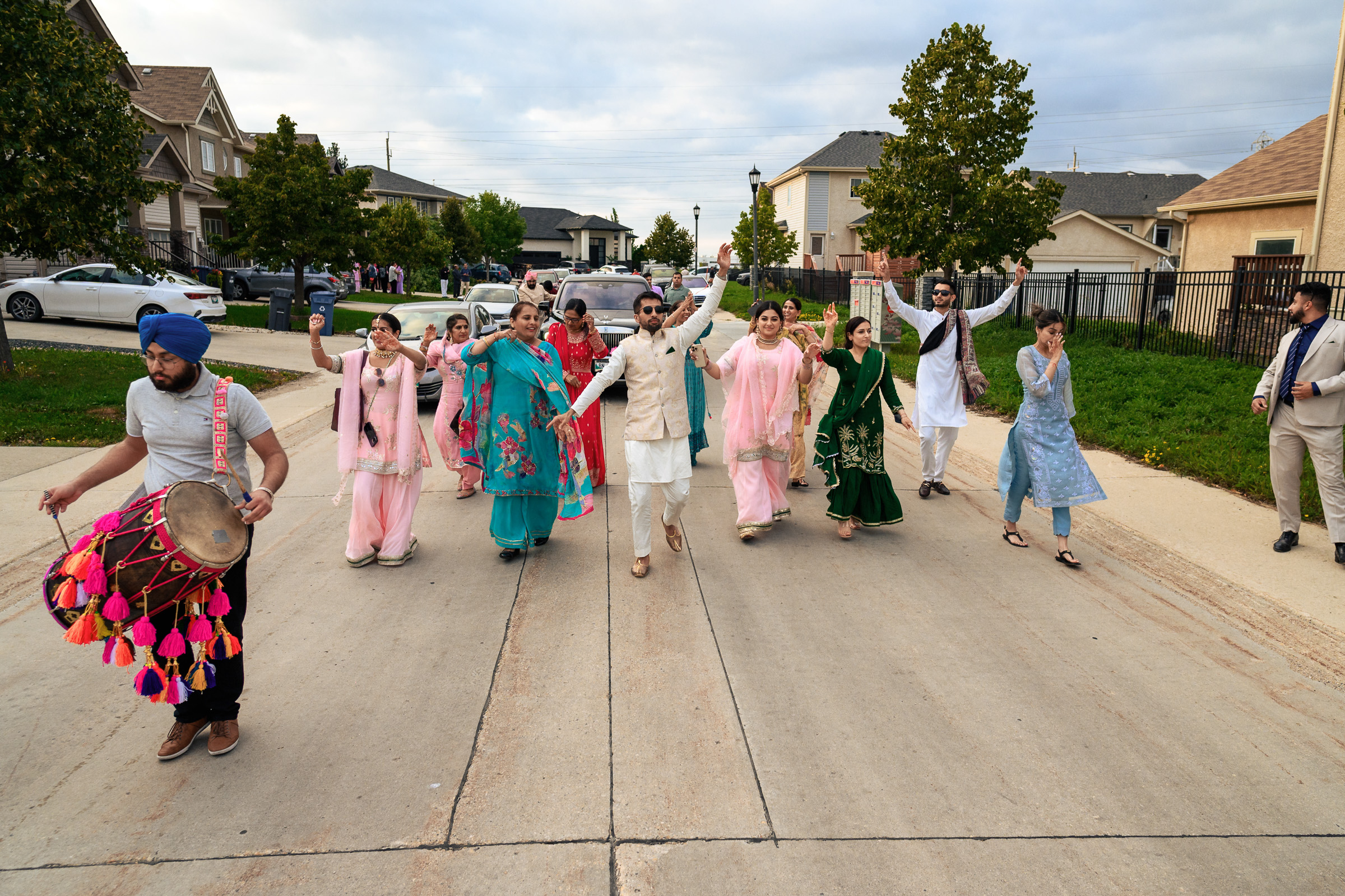 A group of people in traditional attire parade joyfully on a residential street.