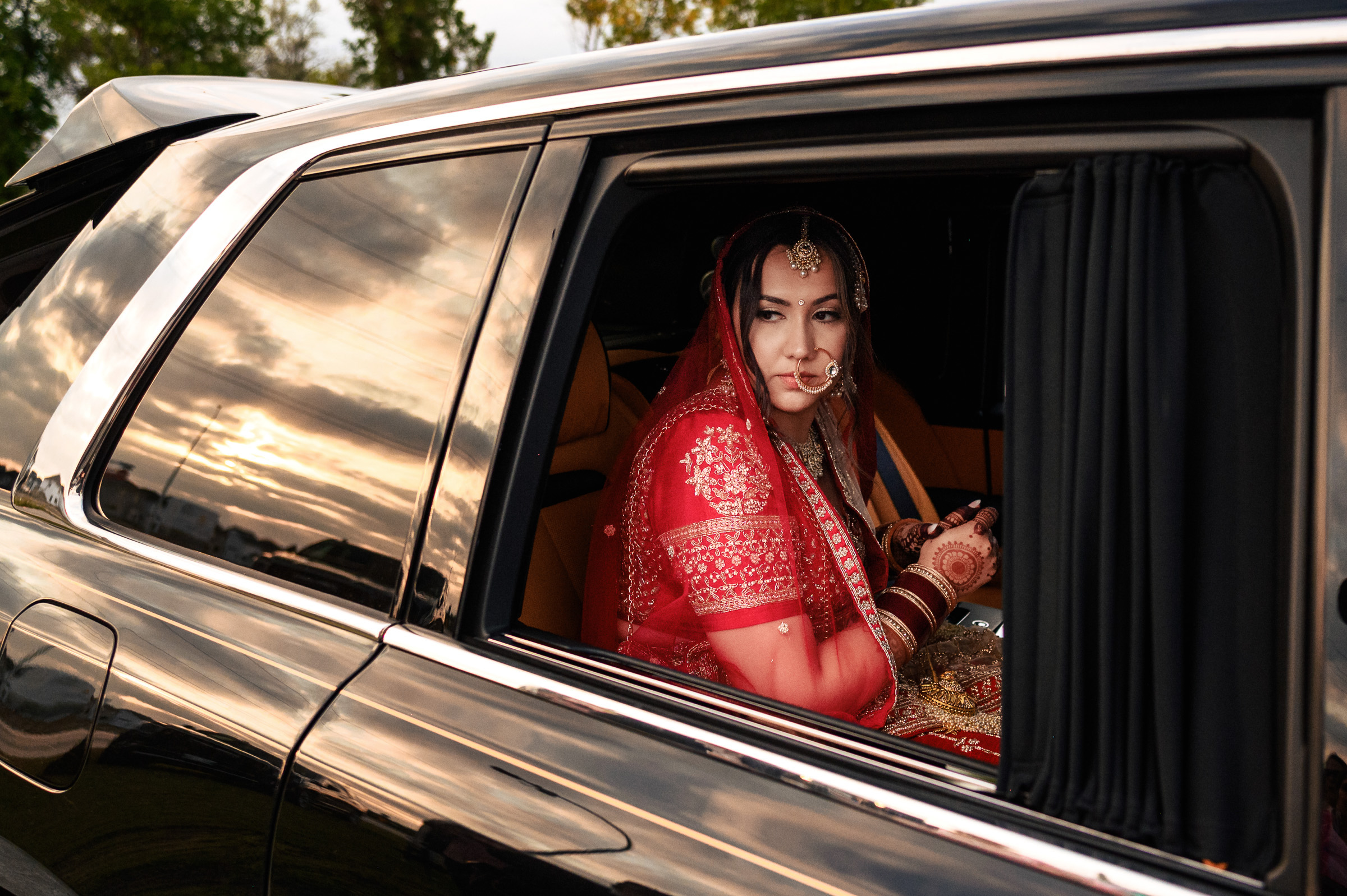 Bride in red traditional attire sitting inside a car, looking out the window.