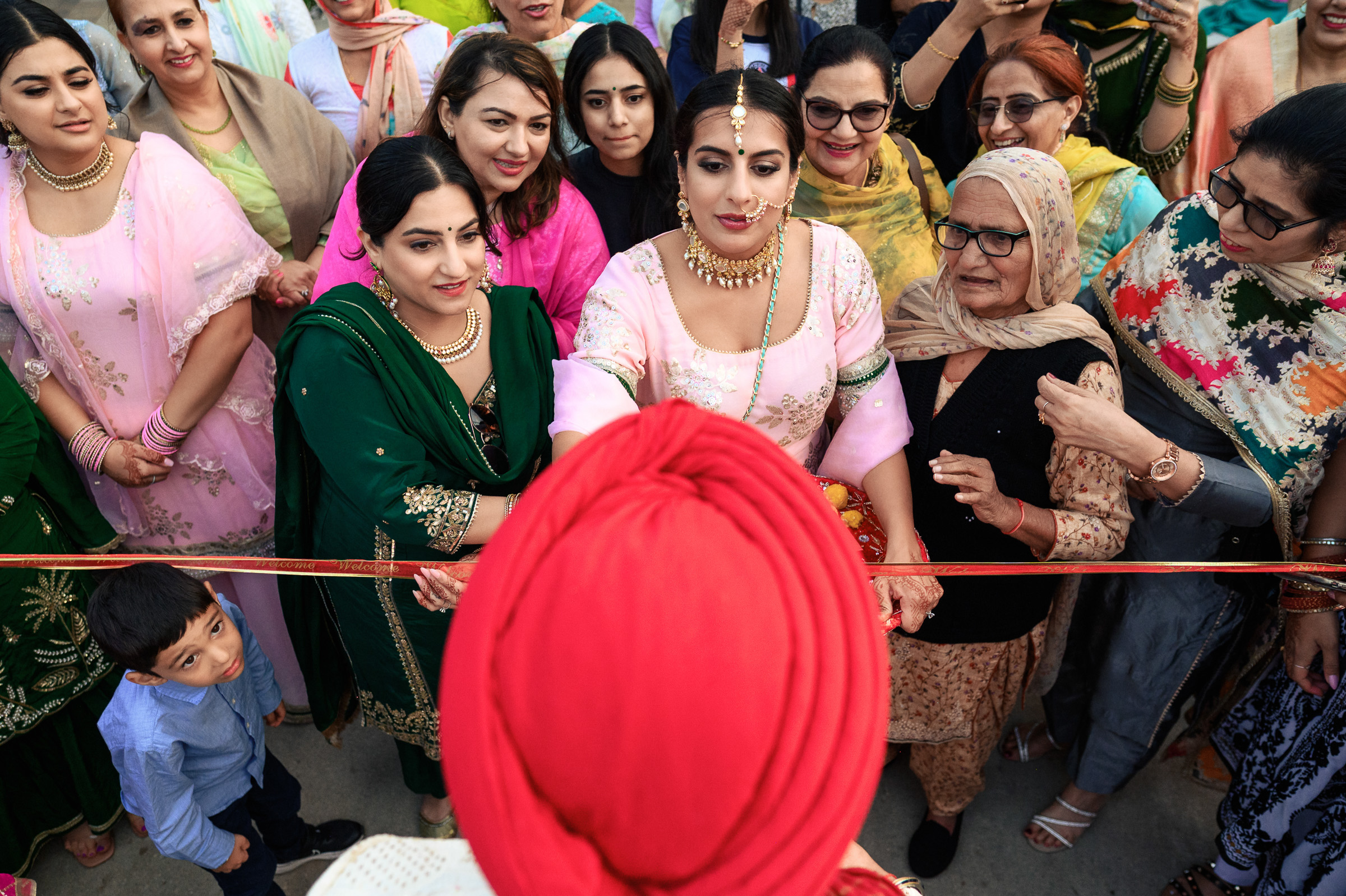 A bride in pink prepares to cut a ribbon, surrounded by family and friends.