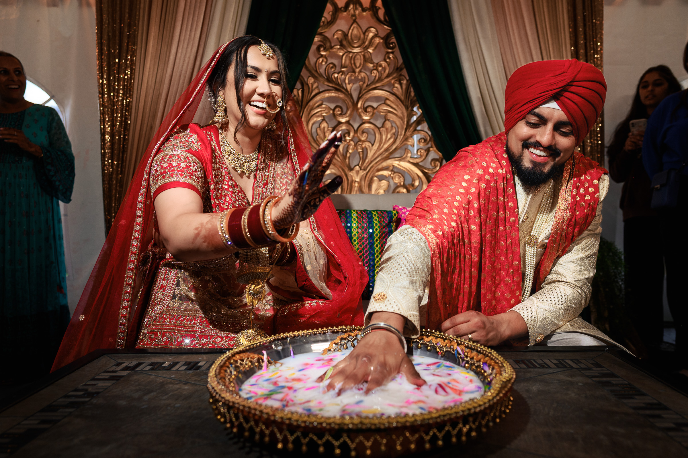 Couple participating in a traditional ceremony, reaching into a bowl with floating petals.